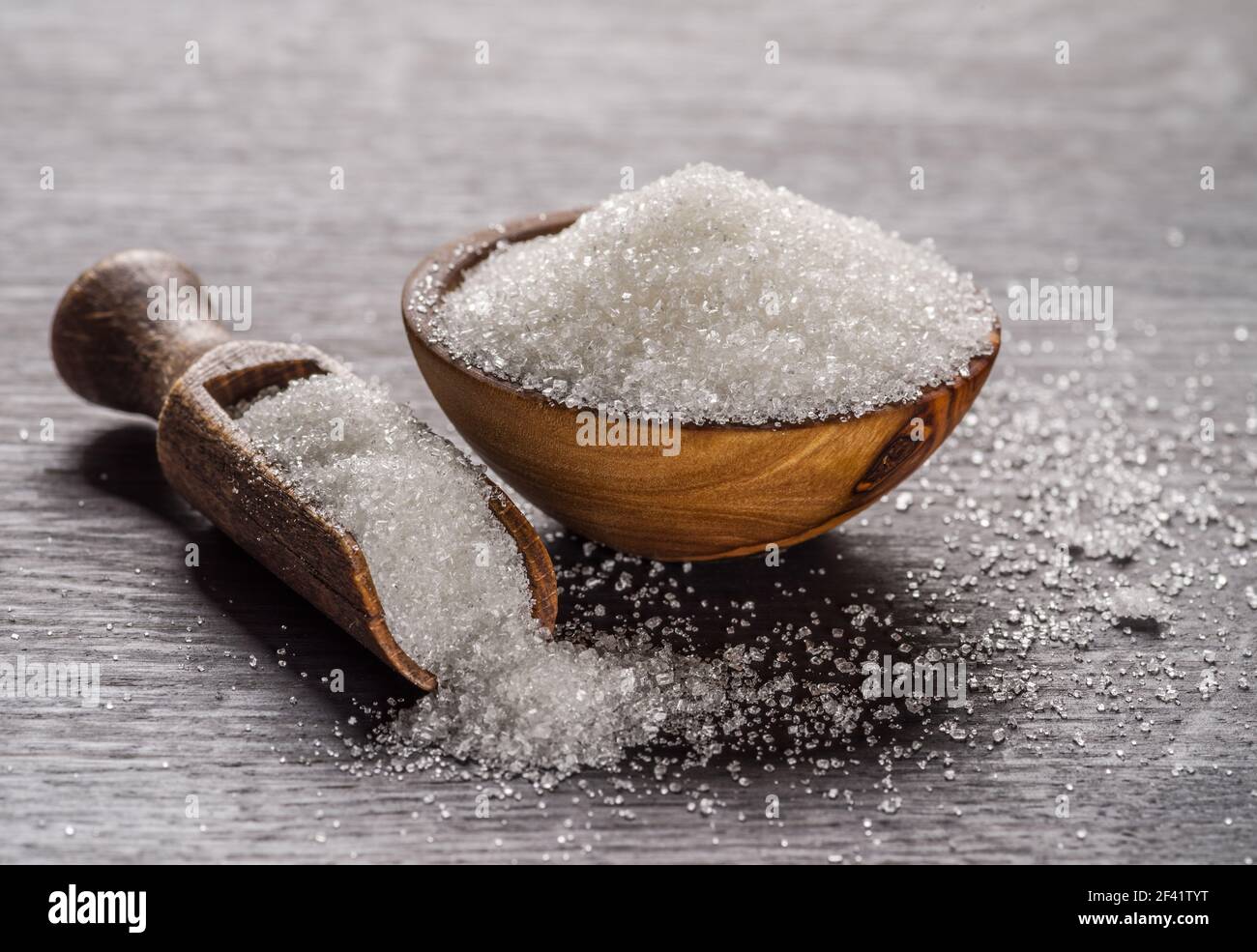 Weißer raffinierter Zucker in Holzschüssel und Löffel auf dunklem Holztisch. Stockfoto