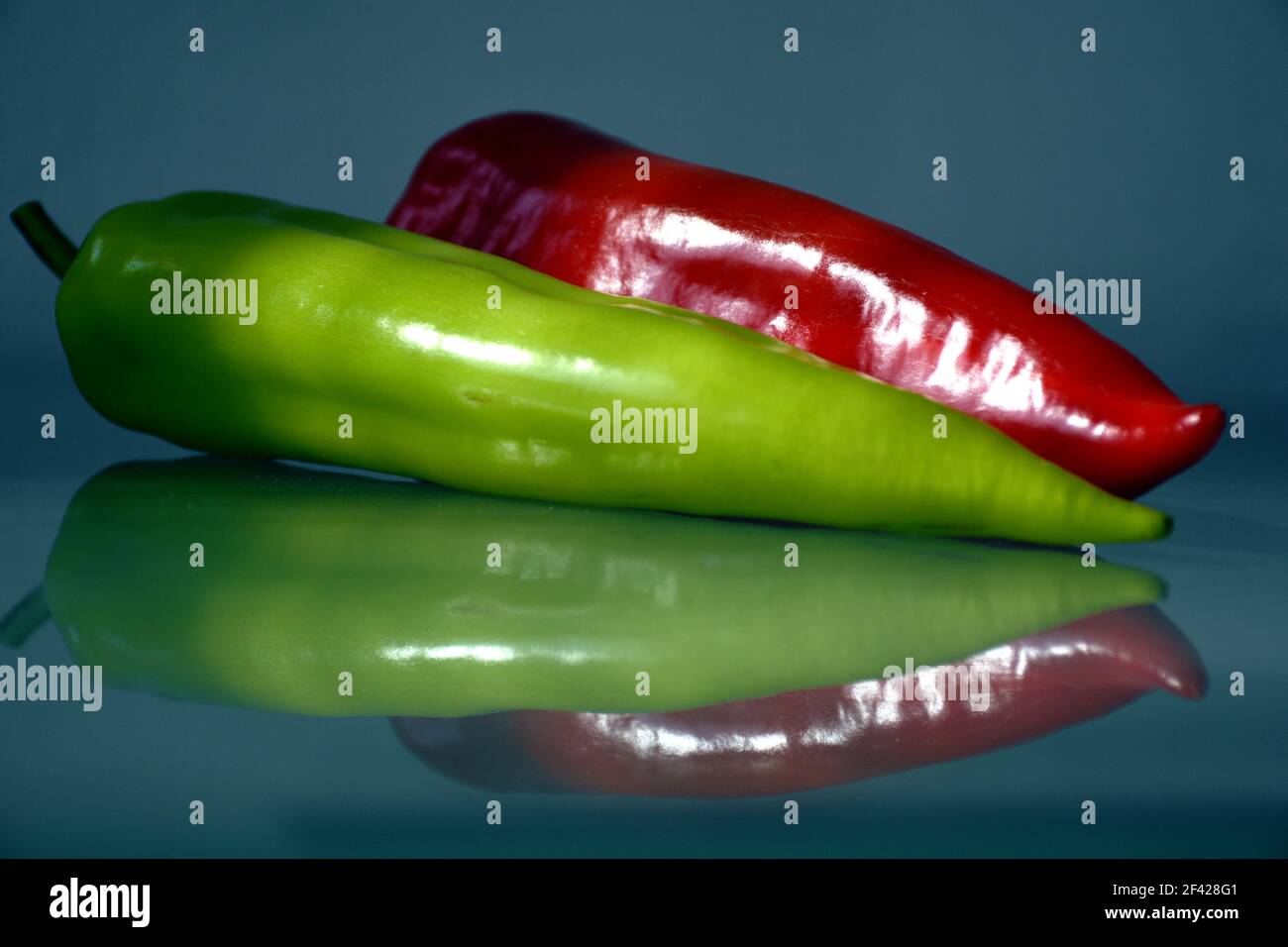 Frische grüne und rote Paprika auf Glasoberfläche. Starke Reflexion. Abstrakte Ansicht. Lebensmittelzutat. Bio-Gemüse. Gesunde Ernährung. Vegane Lebensart. Stockfoto