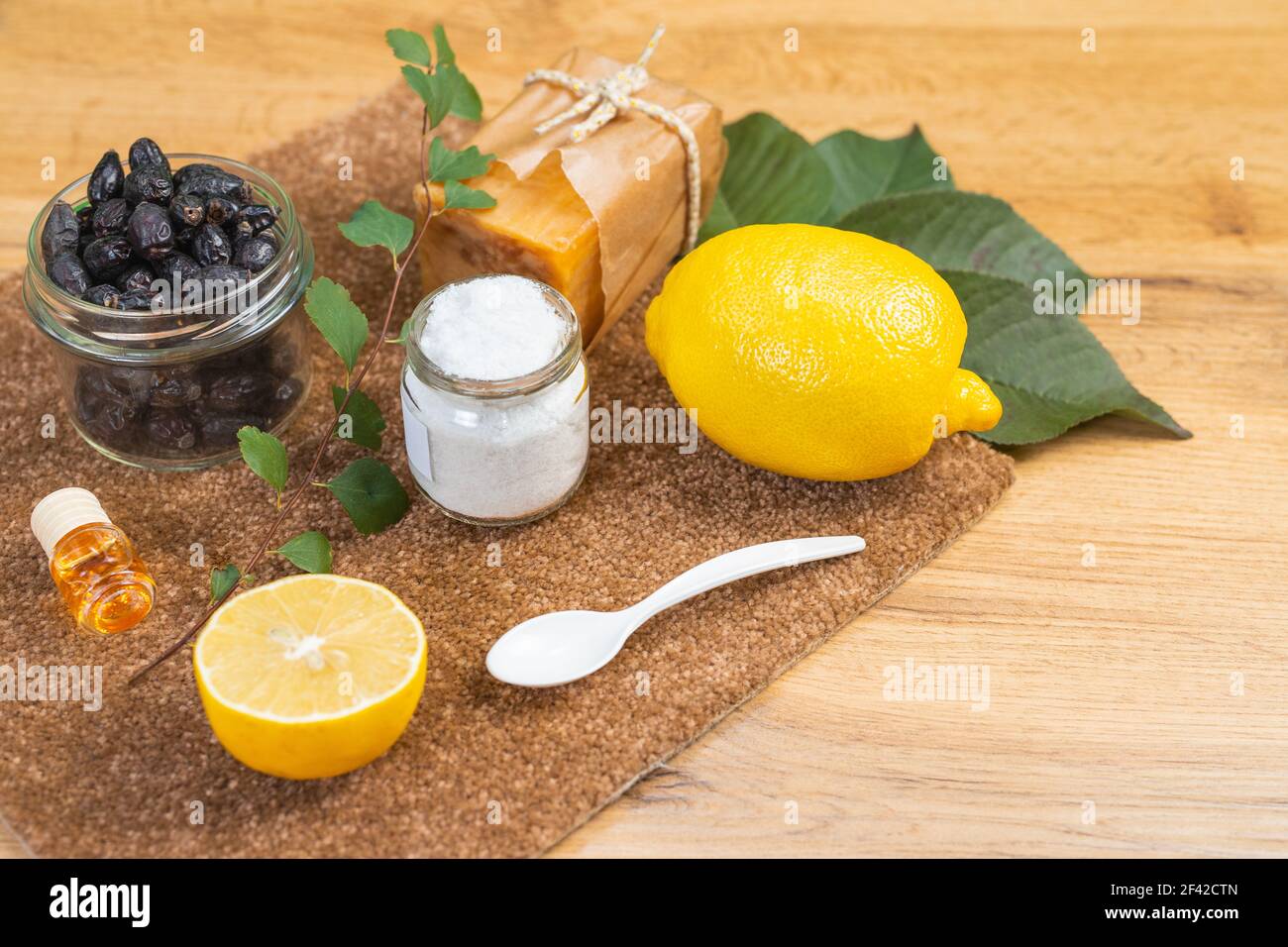Ökologische natürliche Reinigungsmittel auf einem Holztisch. Natürliche Seife, Zitrone, Öl, Salz und getrocknete Beeren. Hausmittel Reinigungskonzept. Stockfoto