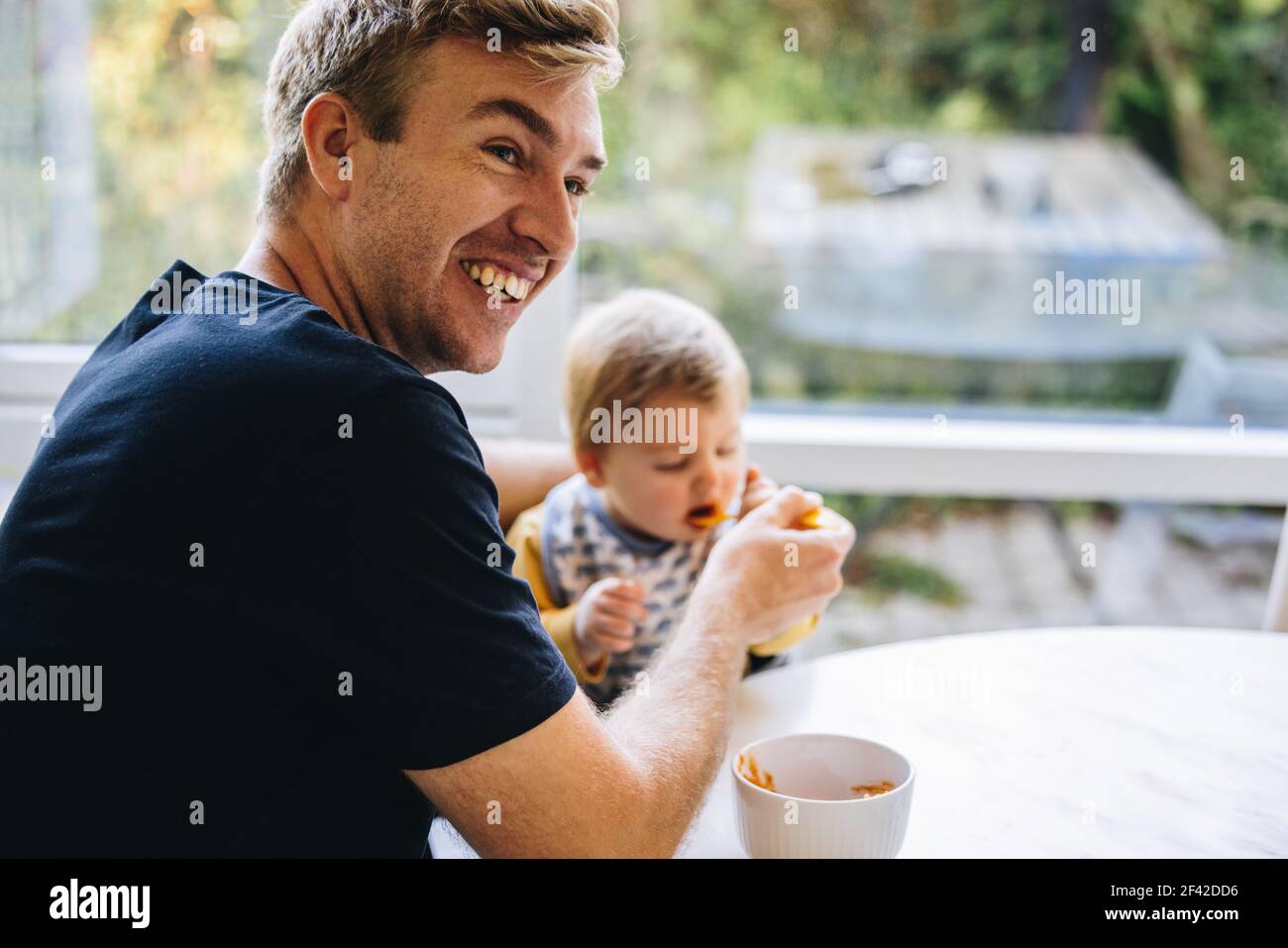 Lächelnder Mann Fütterung Baby mit Löffel, Vater kümmert sich um sein Baby, während in Vaterschaft verlassen. Stockfoto