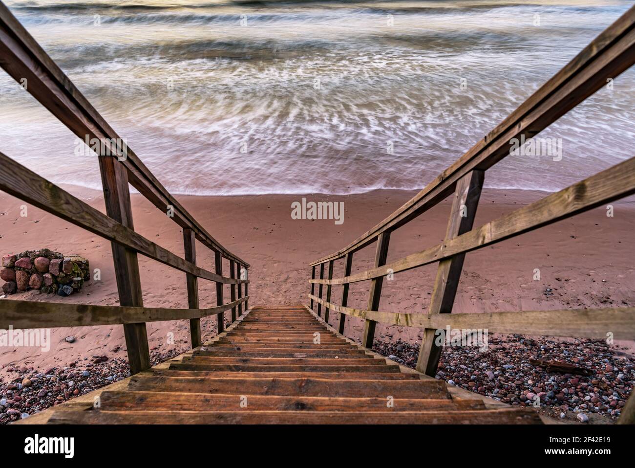 Eine Holztreppe, die es Ihnen ermöglicht, zum Strand zu gelangen, ganz in der Nähe der Küste des Wassers, genau wie direkt in das Meerwasser zu gehen Stockfoto