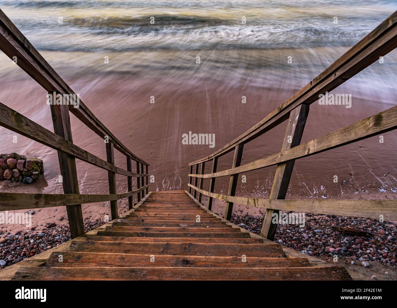 Eine Holztreppe, die es Ihnen ermöglicht, zum Strand zu gelangen, ganz in der Nähe der Küste des Wassers, genau wie direkt in das Meerwasser zu gehen Stockfoto