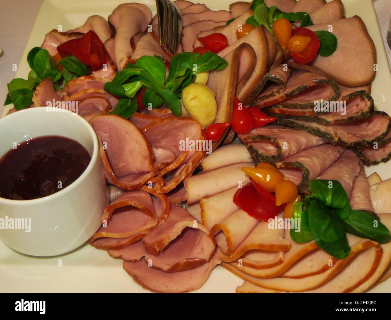 Vorspeise aus verschiedenen Fleischprodukten, garniert mit Kirschtomaten und Kräutern. Geräucherter und gekochter Schinken Stockfoto