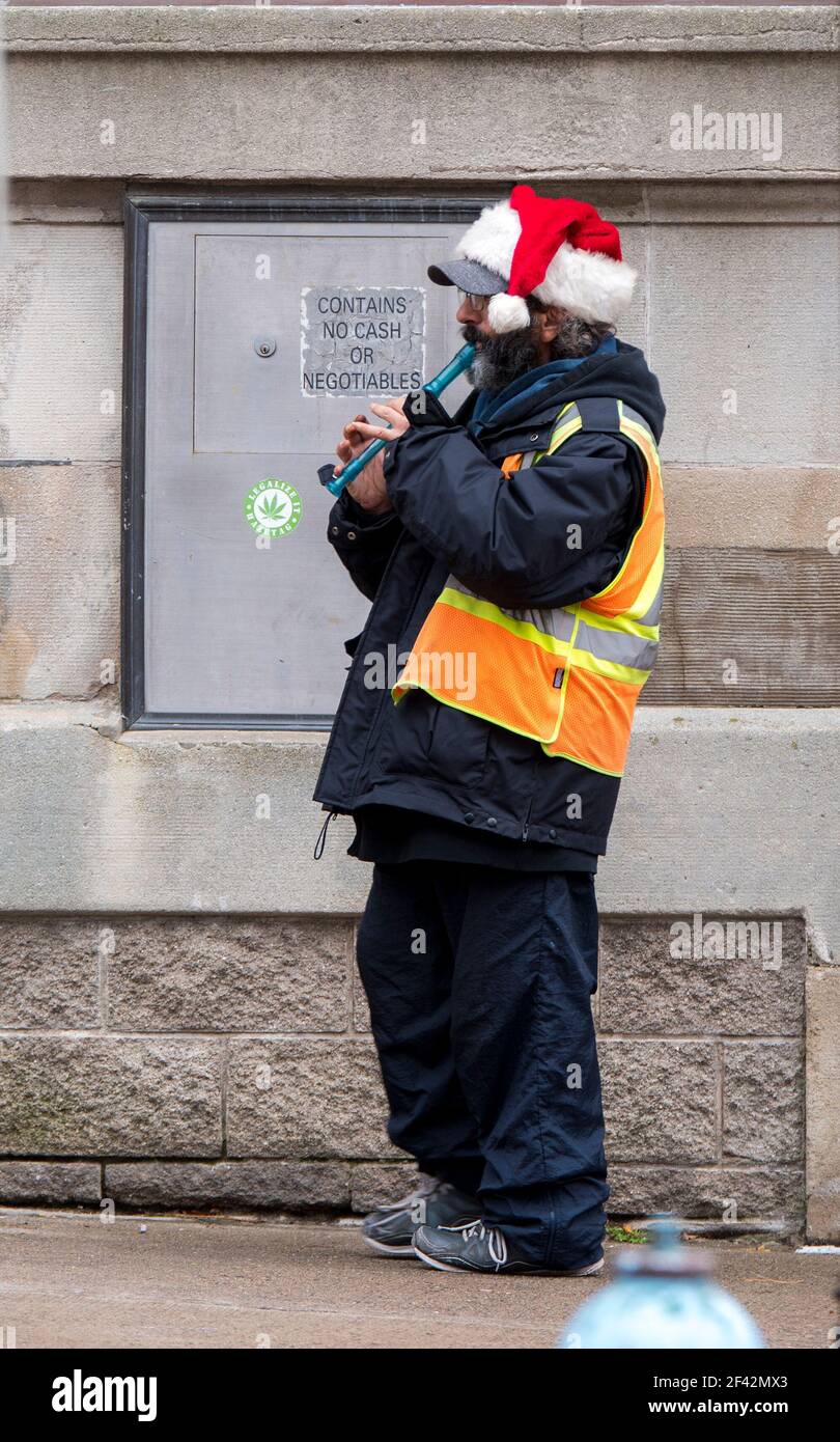 Saint John, New Brunswick, Kanada - 26. November 2017: Ein Mann, der auf einem Bürgersteig steht und eine Blockflöte spielt. Er trägt einen Weihnachtsmann Hut und Sicherheitsweste. Stockfoto