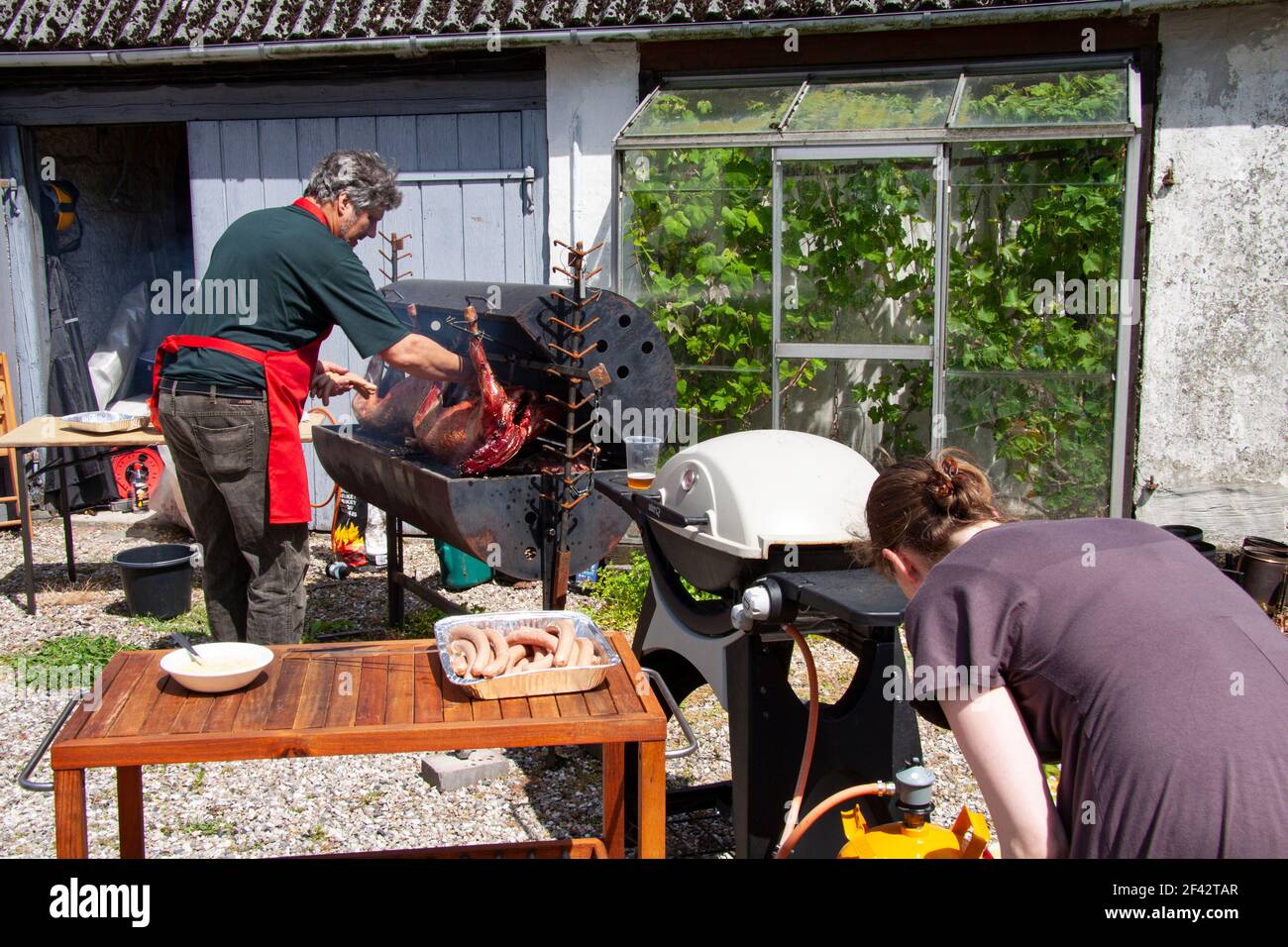 Mann und Frau braten ganze Schweine und Würstchen auf Außengrill. Stockfoto