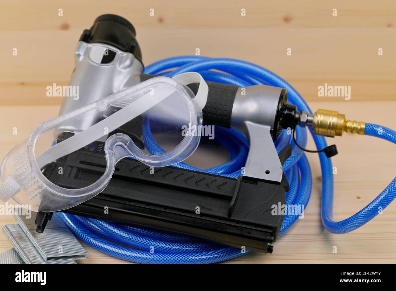 Ein Druckluftnagler mit Druckschlauch, Schutzbrille und Klammerhalterungen Stockfoto