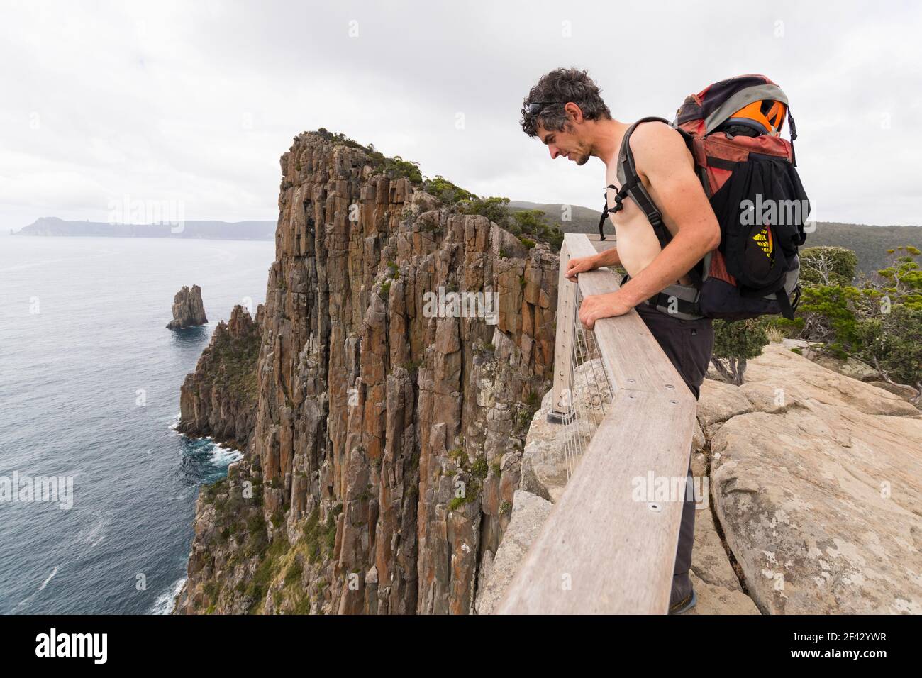 Der Mann, der einen Rucksack trägt, lehnt sich über die Klippen Tasmaniens. Stockfoto