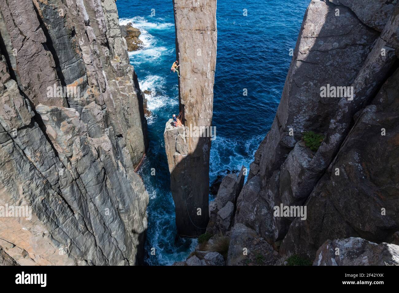 Frau klettert auf einen frei stehenden Felsen pilar, der aus dem Meer auftaucht. Stockfoto