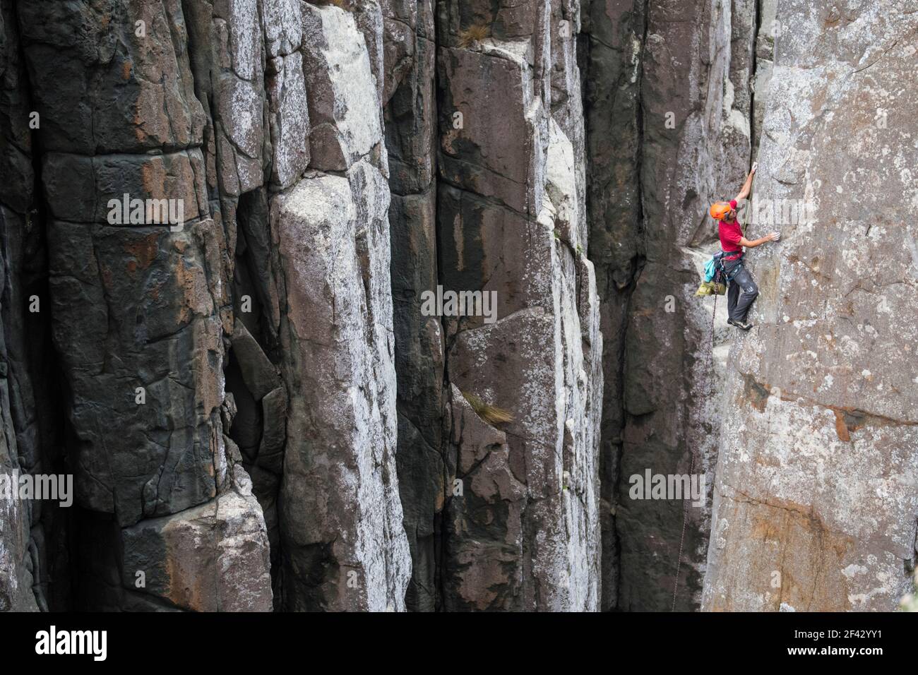 Der Kletterer mit rotem Hemd macht sich auf den Weg am Rand einer Dolerit-Felssäule im Totem Pole, Cape Hauy, Tasman National Park, Tasmanien, Australien. Stockfoto