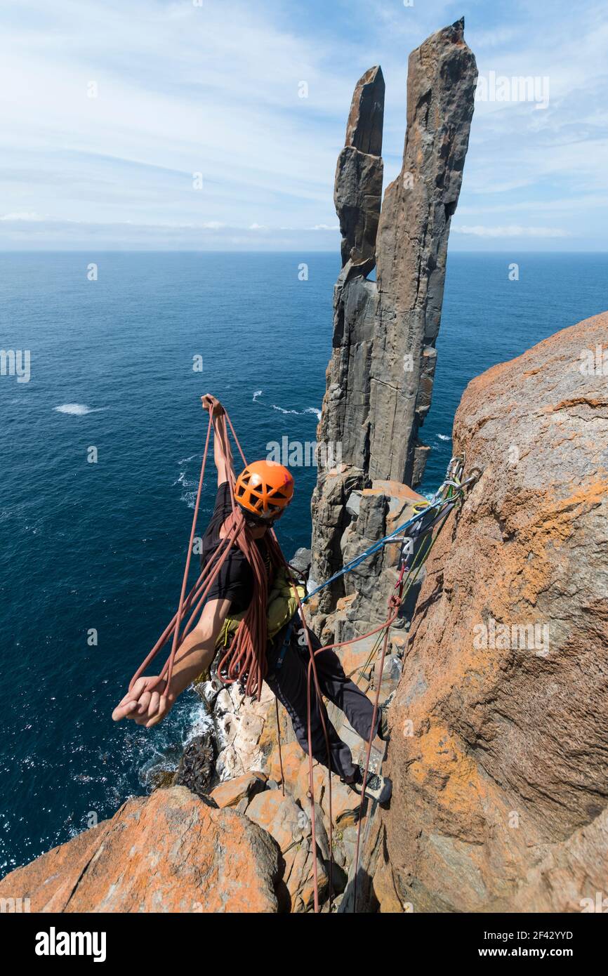 Männlicher Abenteurer wickelt das Seil auf, während er seine nächste Herausforderung umgeht: Zwei freistehende Felspilaren, die aus dem Meer in den Meeresklippen von Cape Raoul in Tasmanien, Australien, aufsteigen. Stockfoto