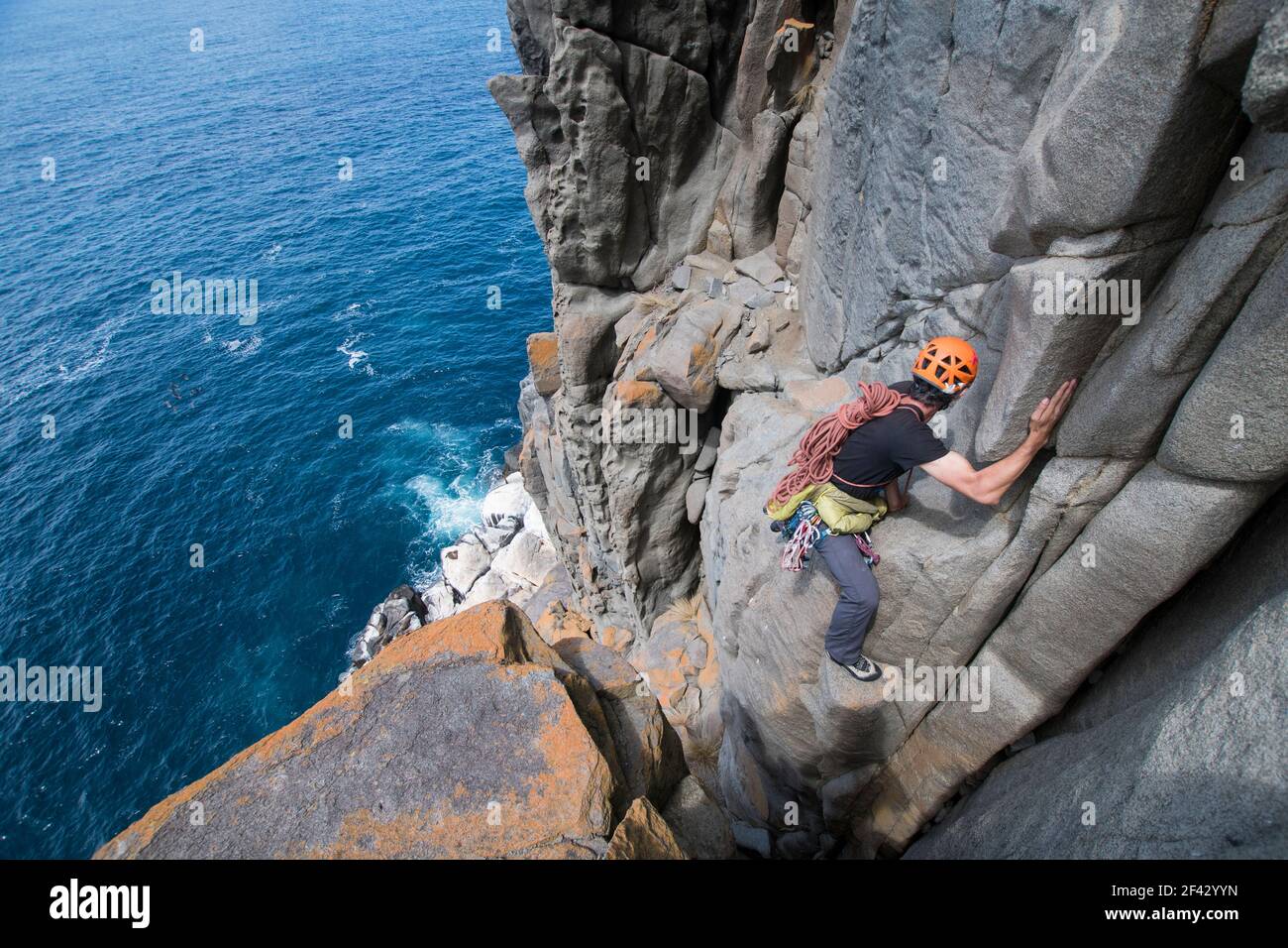 Der männliche Abenteurer geht mit Seilen und Kletterausrüstung in den Uneigenen, während er Dolerit-Felskolonnen in den Meeresklippen von Cape Raoul in Tasmanien, Australien, erkundet. Stockfoto