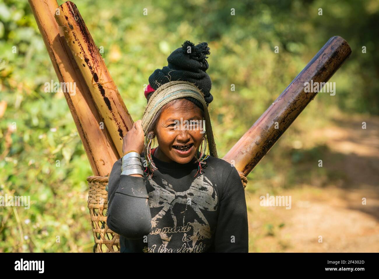 Porträt einer erwachsenen Frau des Stammes der Engstämme, die Bambusstämme im Packkorb trägt, in der Nähe von Kengtung, Myanmar Stockfoto