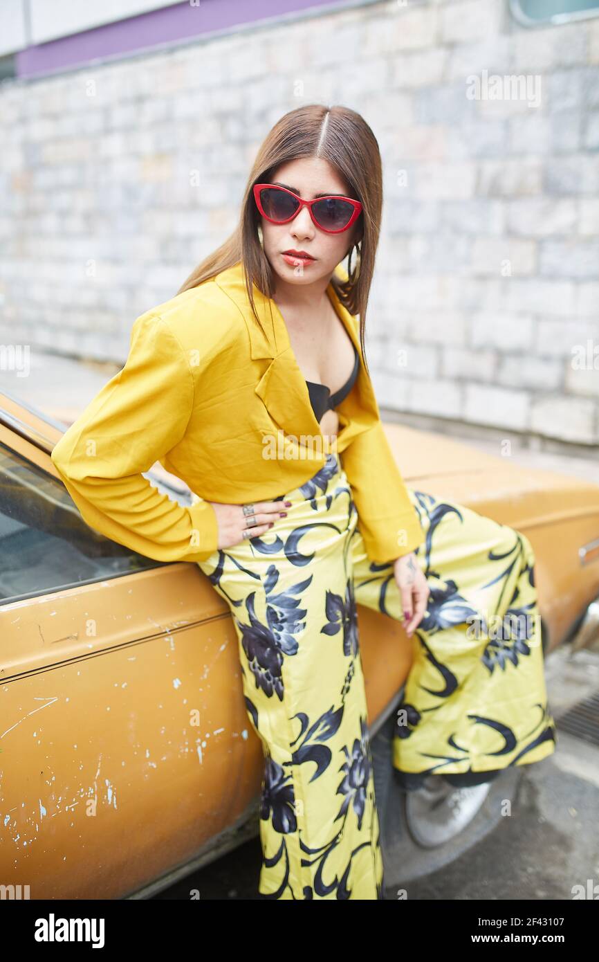 Junge Frau in gelbem Kleid, die sich gegen ein Auto lehnt Stockfoto