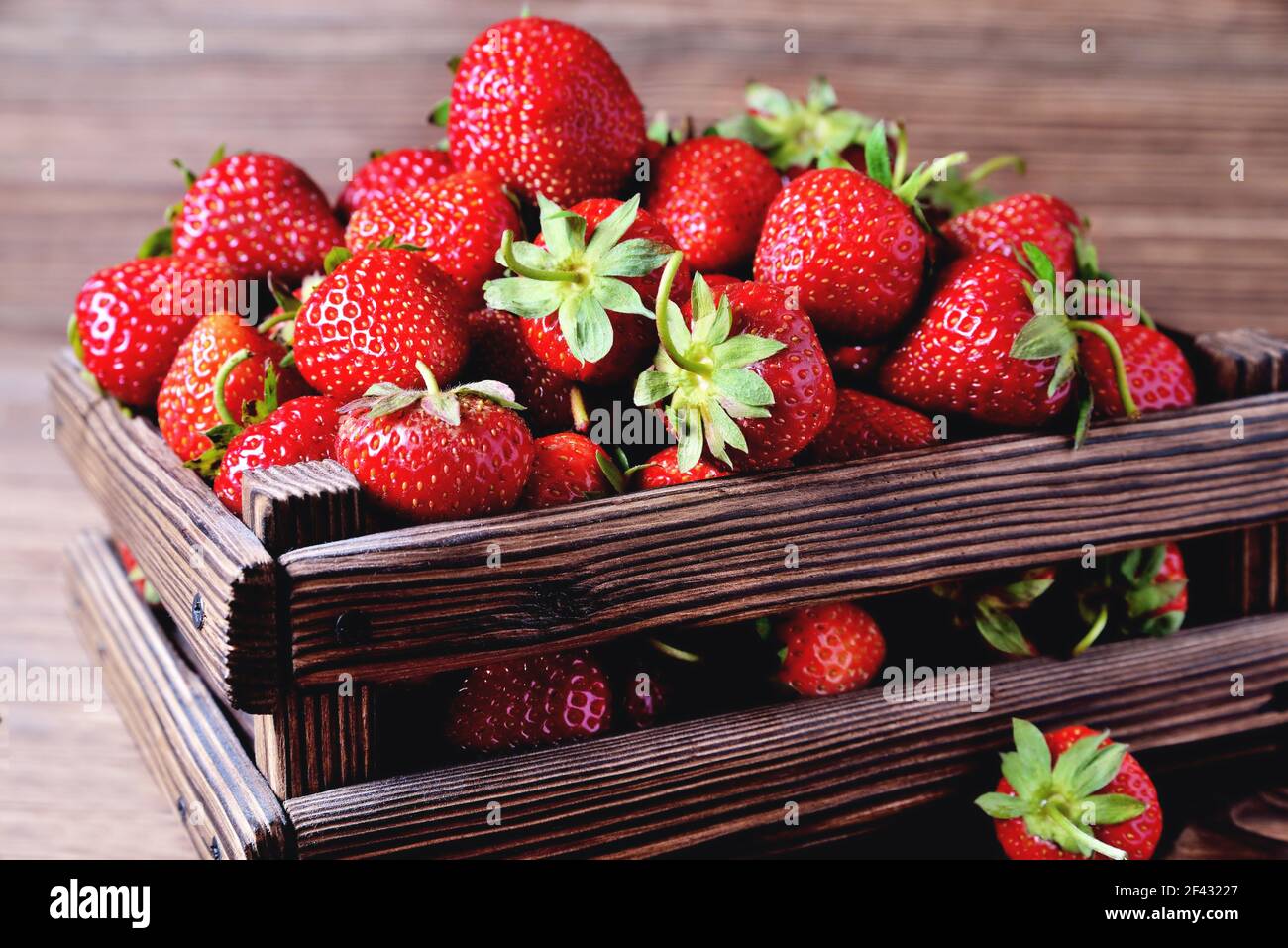 Erdbeeren in einer Holzkiste auf einem natürlichen Holzhintergrund, verschwimmen als künstlerische Technik des Autors close-up copy space Stockfoto