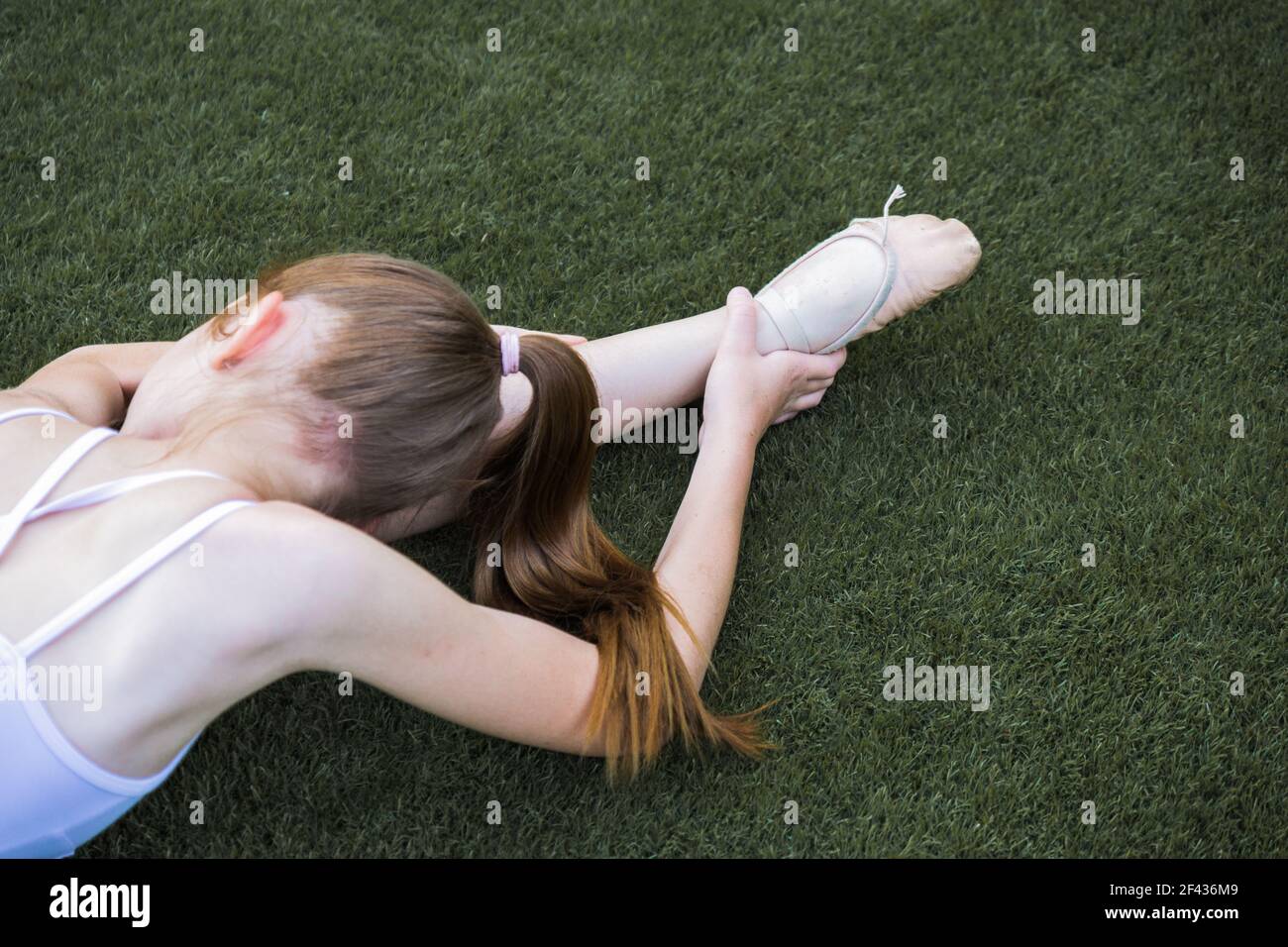 Balletttänzerin Mädchen Stretching auf dem Grasboden mit ihr Kopf zu einer Seite und rothaarige Pferdeschwanz Stockfoto