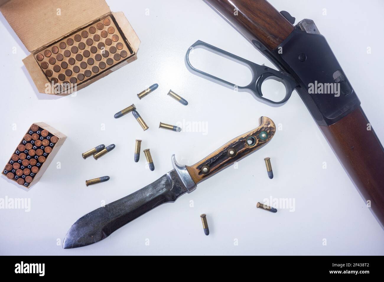 Jagdkonzept mit einem Hebelgewehr, einem mit Knochen gehandhabten Jagdmesser und .22 Kaliber Geschosse verstreut und in einer Box auf weißem Hintergrund. Stockfoto