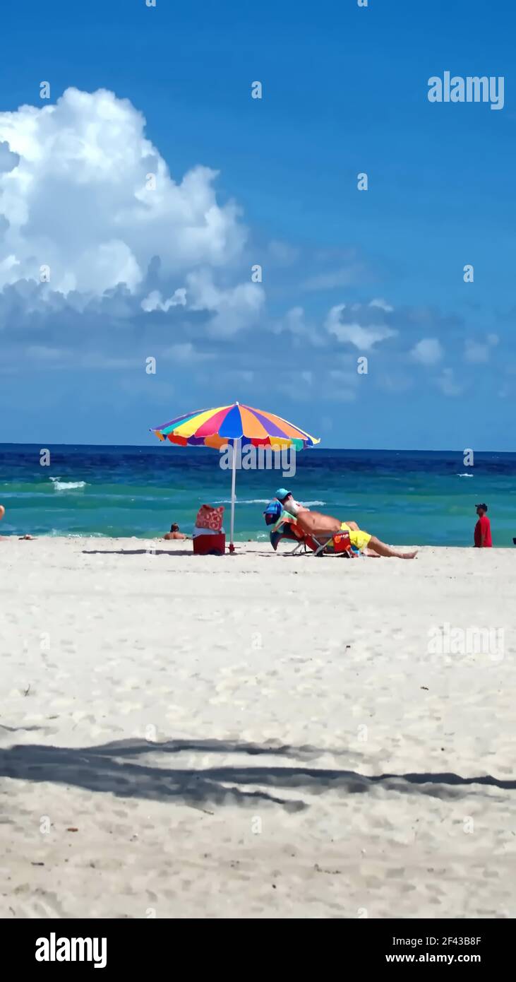Touristen unter einem bunten Sonnenschirm am Dania Beach, Fort Lauderdale, Florida, USA Stockfoto