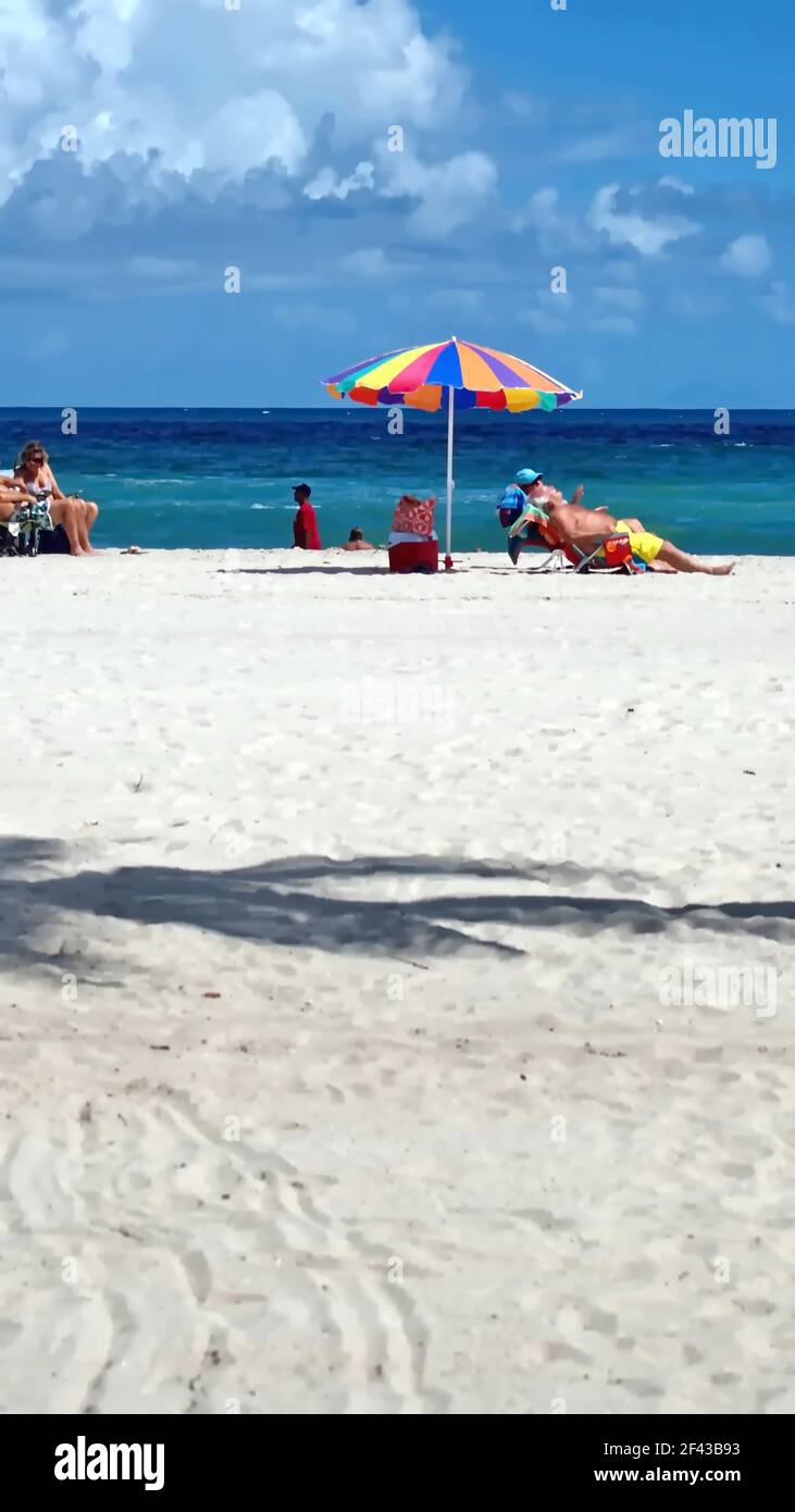 Touristen unter einem bunten Sonnenschirm am Dania Beach, Fort Lauderdale, Florida, USA Stockfoto