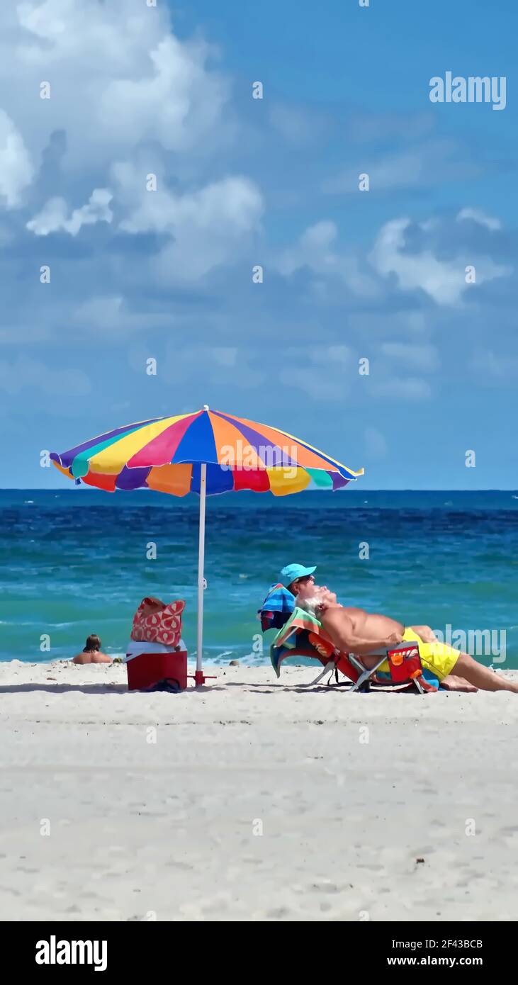 Touristen unter einem bunten Sonnenschirm am Dania Beach, Fort Lauderdale, Florida, USA Stockfoto