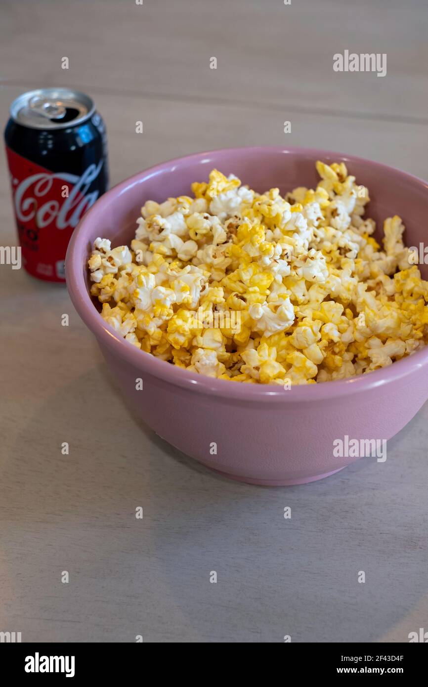 Popcorn oder Popcorn, in einer rosa Schüssel Einstellung auf einem Tisch mit einer Dose Cola Zero, eine Diät kohlensäurehaltige Getränk. Stockfoto