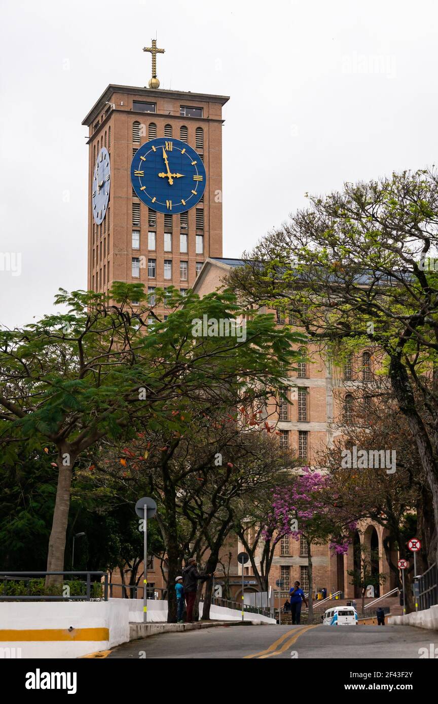 Der Uhrenturm von der Basilika unserer Lieben Frau von Aparecida sah von einer Zufahrtsstraße des religiösen Komplexes, hinter Bäumen und unter bewölktem Himmel. Stockfoto