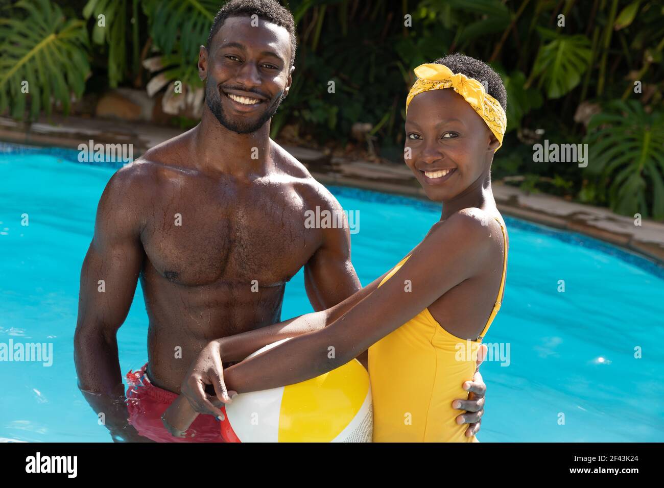 Portrait eines afroamerikanischen Paares im Schwimmbad am Strand Ball auf sonniger Gartenterrasse Stockfoto