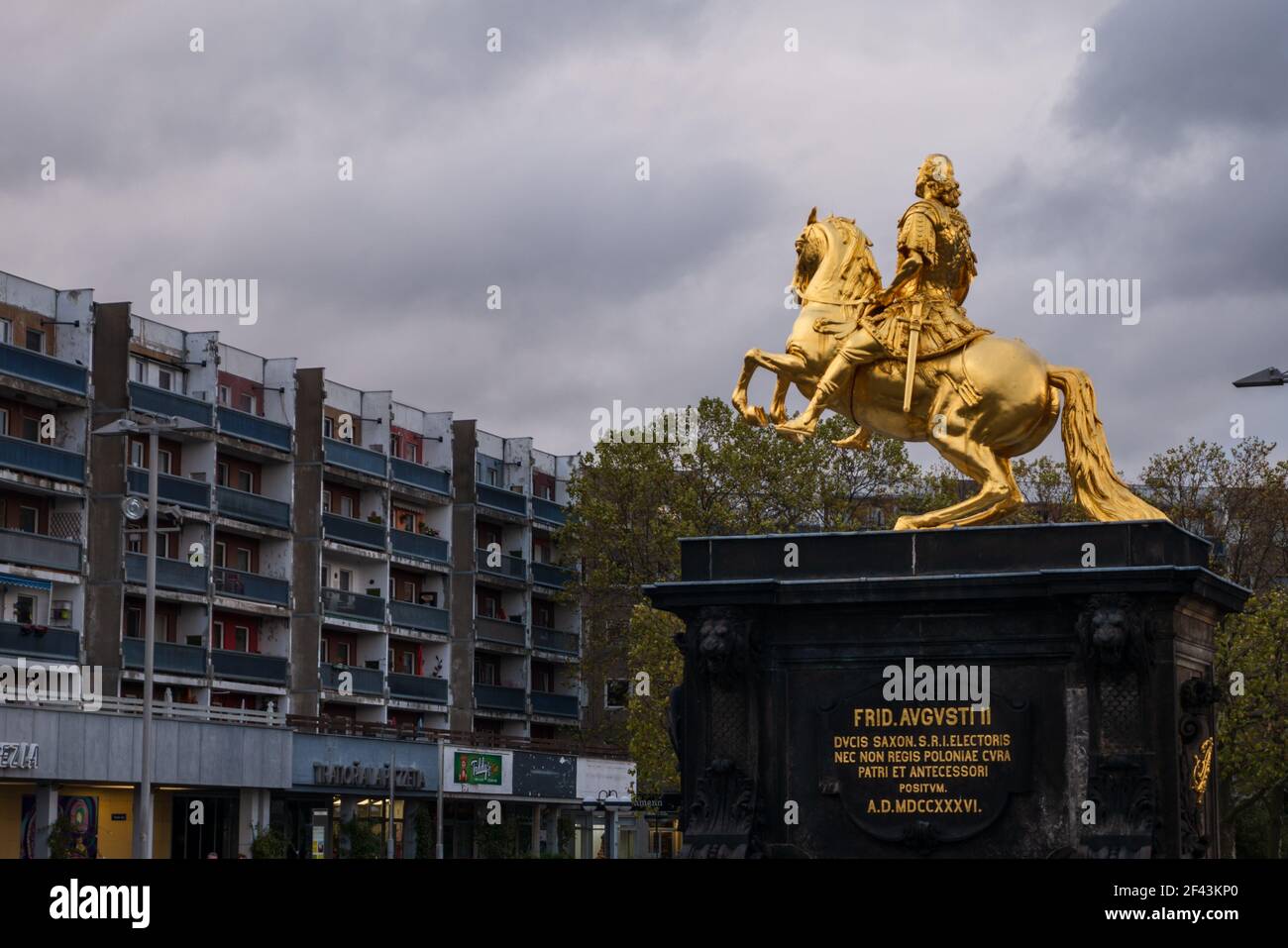 Goldener Reiter August die starke Statue vor alten kaputten Wohngebäuden der DDR. Ein dramatischer Wolkenhimmel ist im Hintergrund. Stockfoto