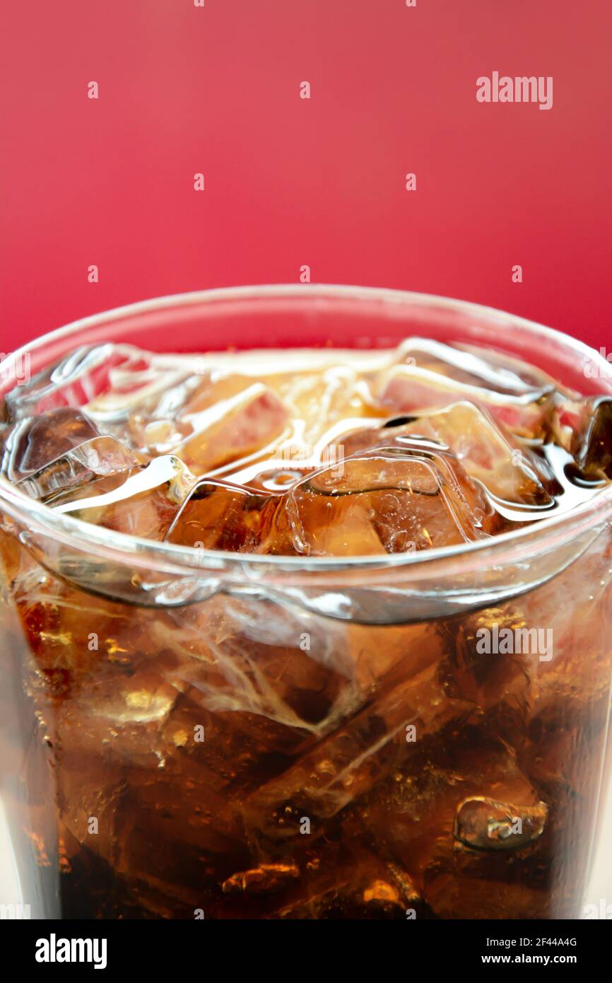 Ein Glas Cola Softdrink mit Eiswürfeln Roter Hintergrund Stockfoto