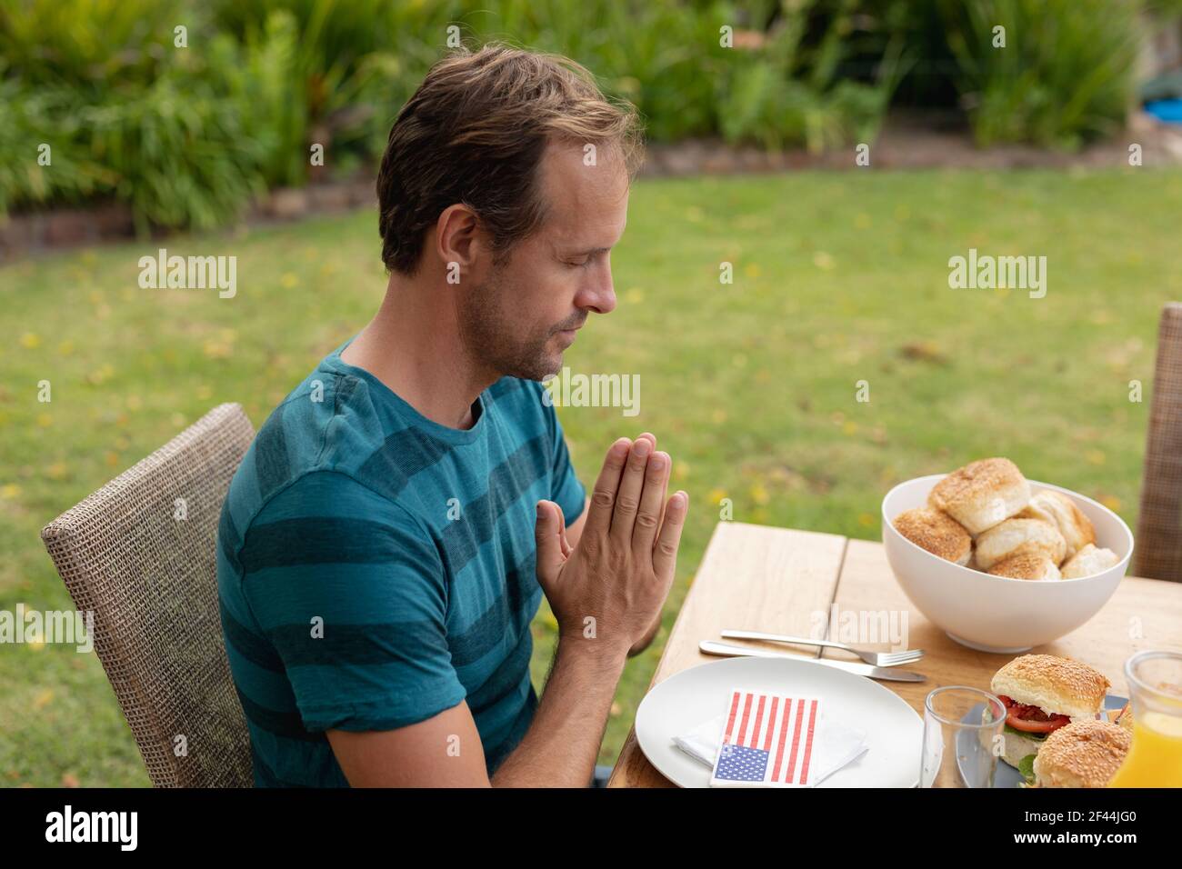 Kaukasischer Mann mit Händen im Gebet sagen Gnade vor dem Essen Essen mit der Familie im Garten Stockfoto
