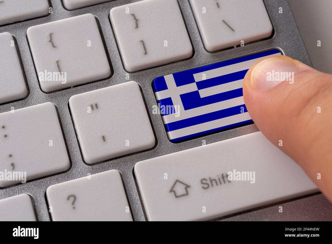 Männliche Hand drücken Tastatur-Taste mit Flagge von Griechenland auf sie. Online internationales Geschäftskonzept. Stockfoto