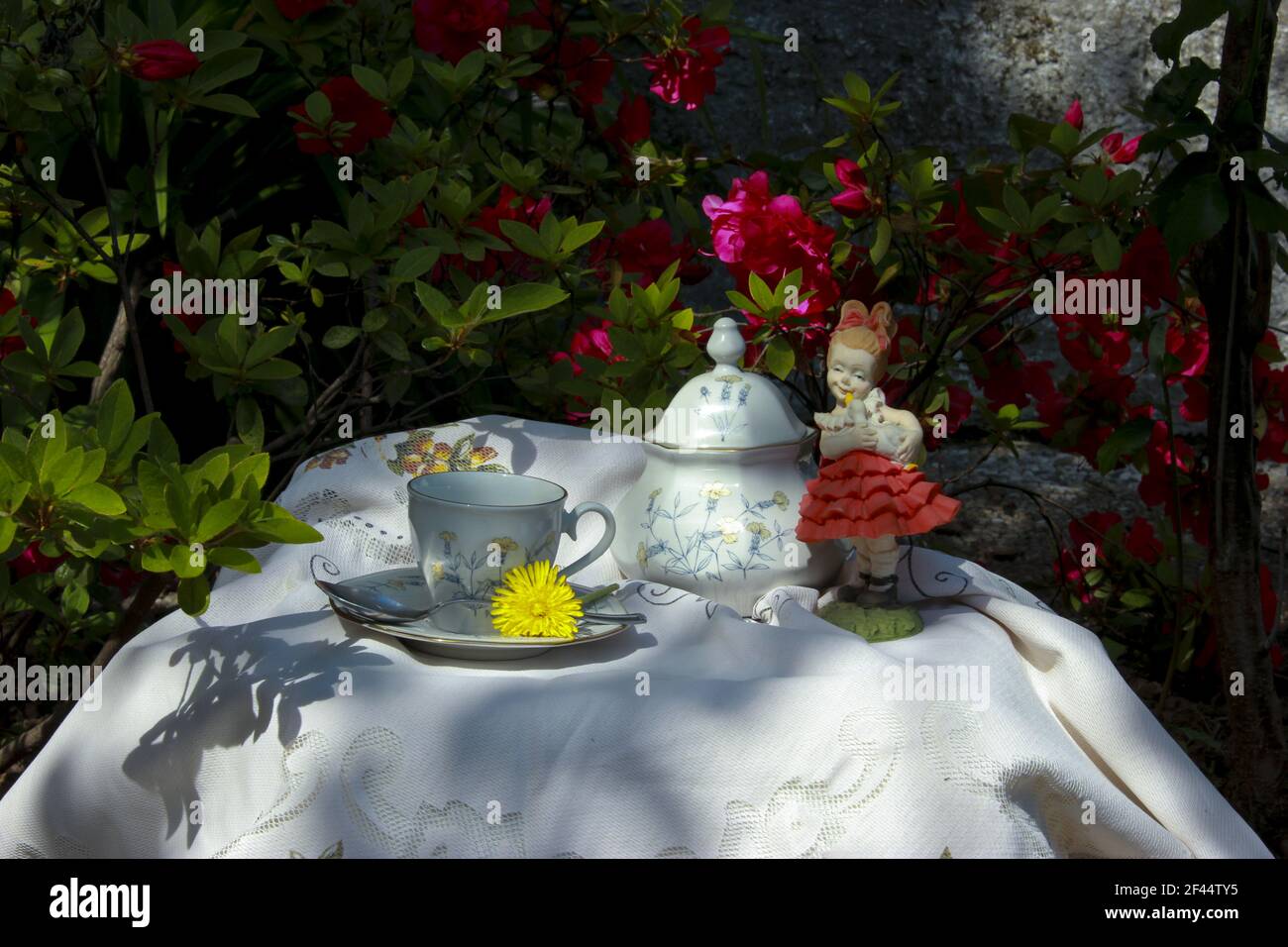 Im Hintergrund eine herrliche Fuchsia Azalea, im Vordergrund ein Tisch für Tee mit antiken Keramiken und einer Porzellanstatuette Stockfoto