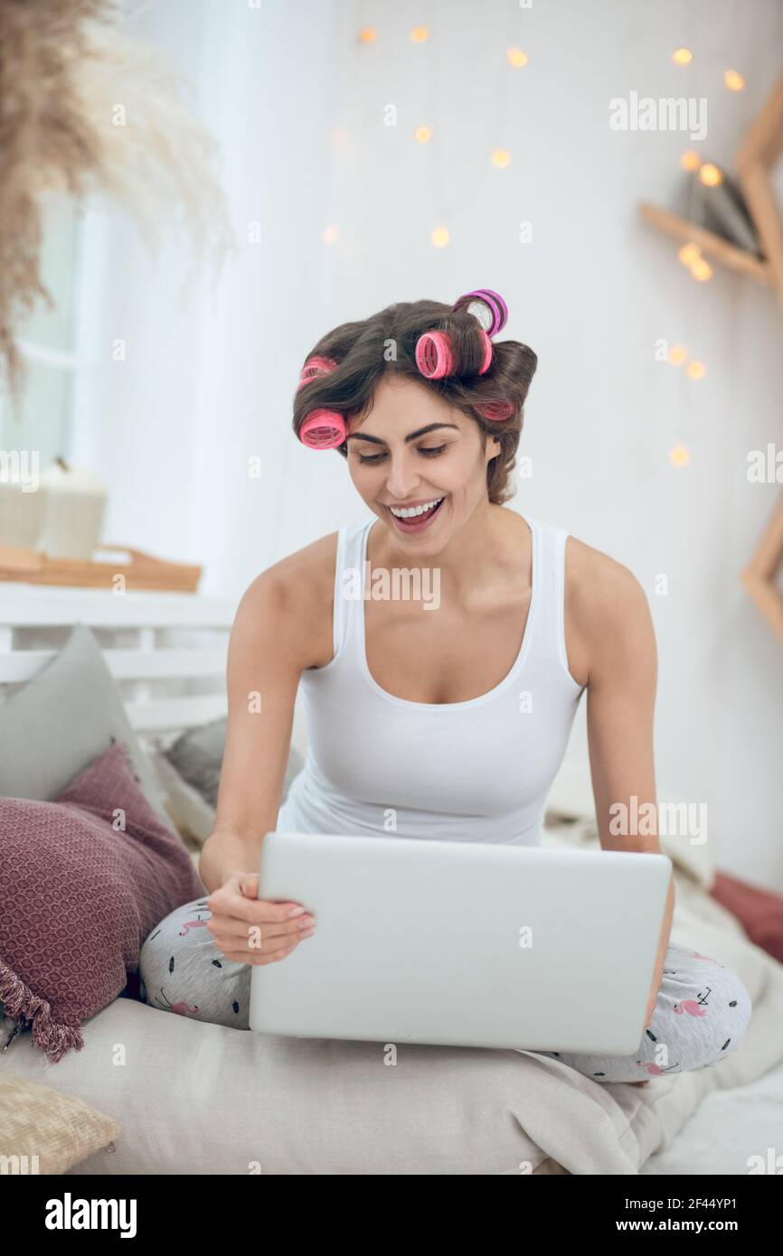 Frau im Haar Lockenwickler sitzen auf dem Bett mit Laptop Stockfoto