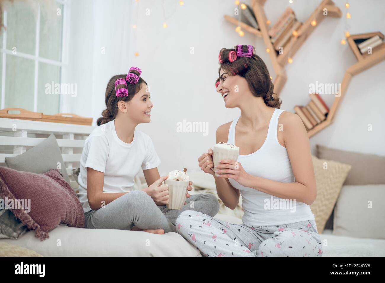Frau und Mädchen in Lockenwickler mit Tassen kommunizieren Stockfoto