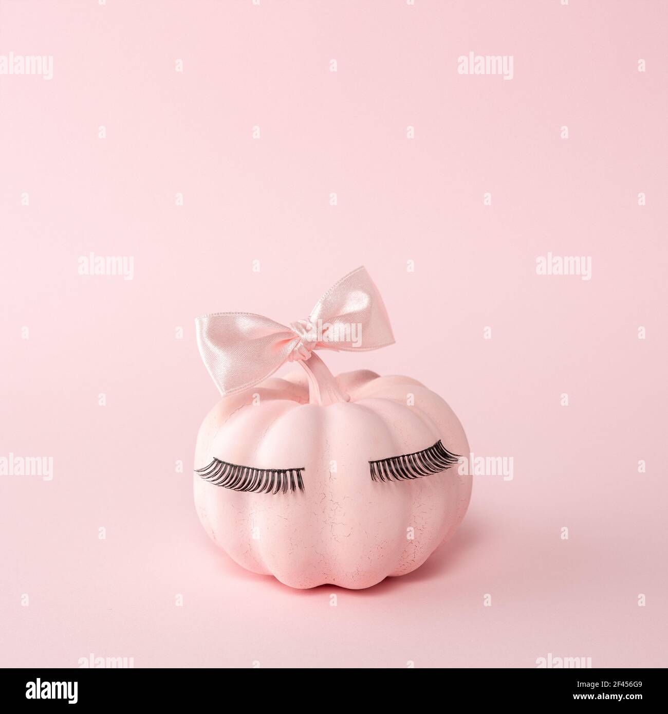 Pinker Halloween Kürbis mit pinker Fliege auf pinkem Hintergrund. Minimal Halloween gruselige Mädchen Konzept. Stockfoto