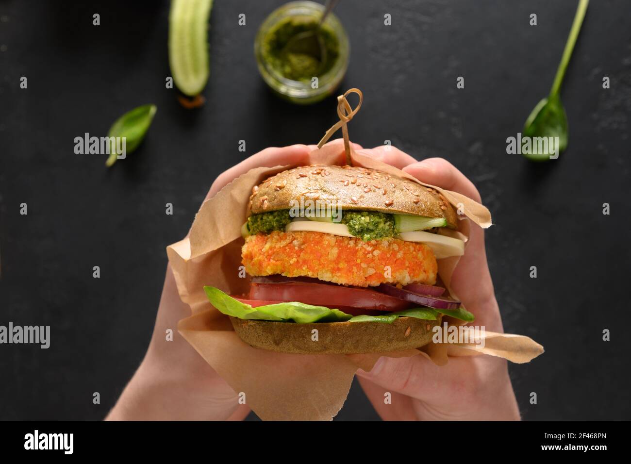 Trendy Vegan Burger von grünen Spirulina Brötchen, Gemüse, veganen Käse, Pesto Karotten Fleischbällchen in den Händen. Nahaufnahme. Horizontale Ausrichtung. Stockfoto