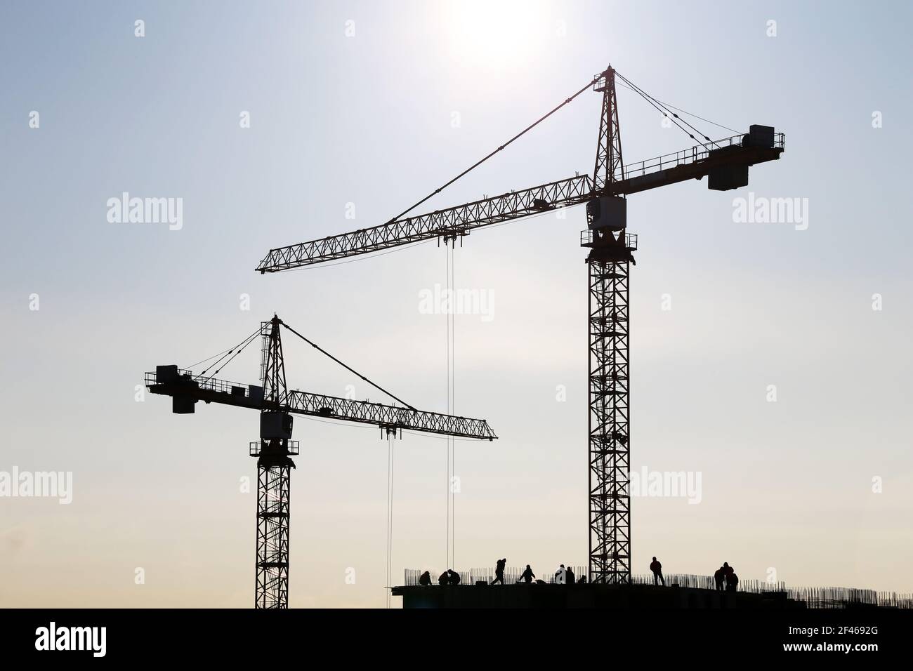 Silhouette von Baukran und Arbeiter auf unfertigen Wohngebäude gegen Sonnenschein. Wohnungsbau, Wohnblock in der Stadt Stockfoto