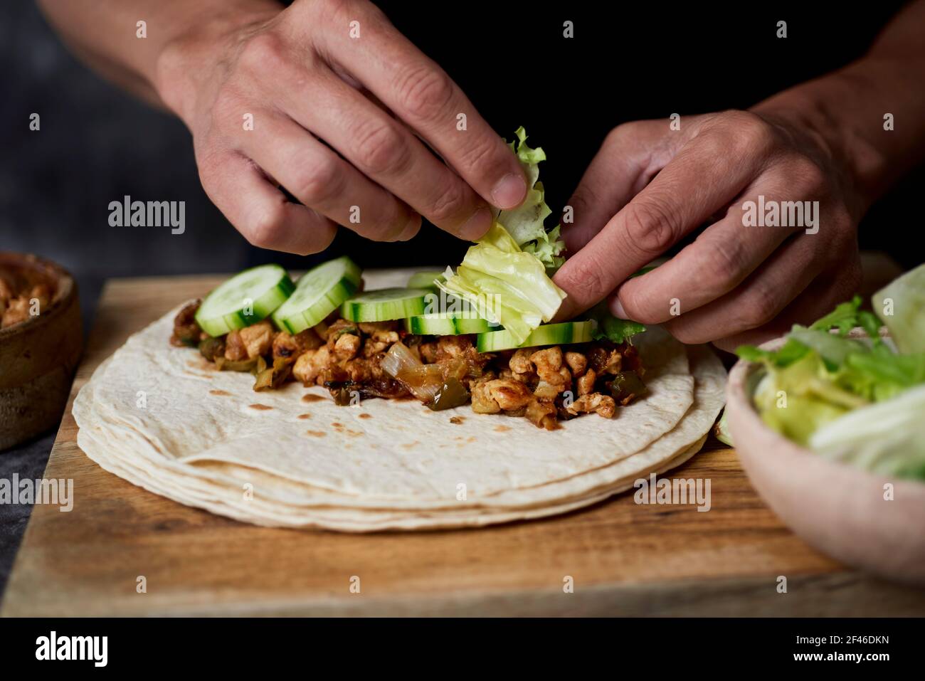 Ein junger Kaukasier füllt ein Durum oder Burrito, mit Hühnerfleisch, das mit Zwiebel und rotem und grünem Pfeffer gekocht wird, und frischem Salat und einigen Scheiben von R Stockfoto