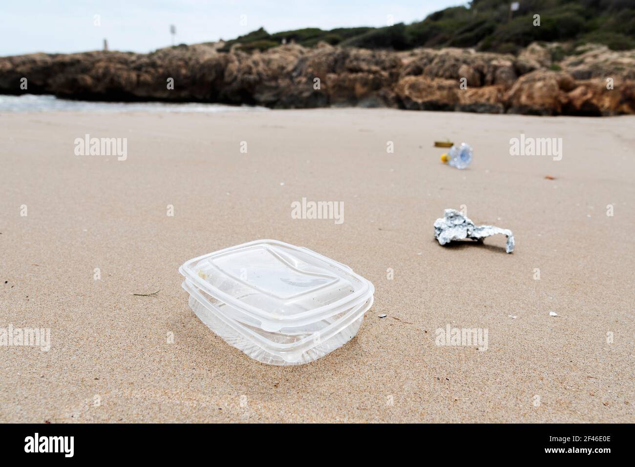 Nahaufnahme eines gebrauchten Plastikbehälters, der auf den nassen Sand eines Strandes geworfen wird, neben anderem Müll, wie ein Stück Aluminiumfolie oder ein gebrauchter Kunststoff Stockfoto