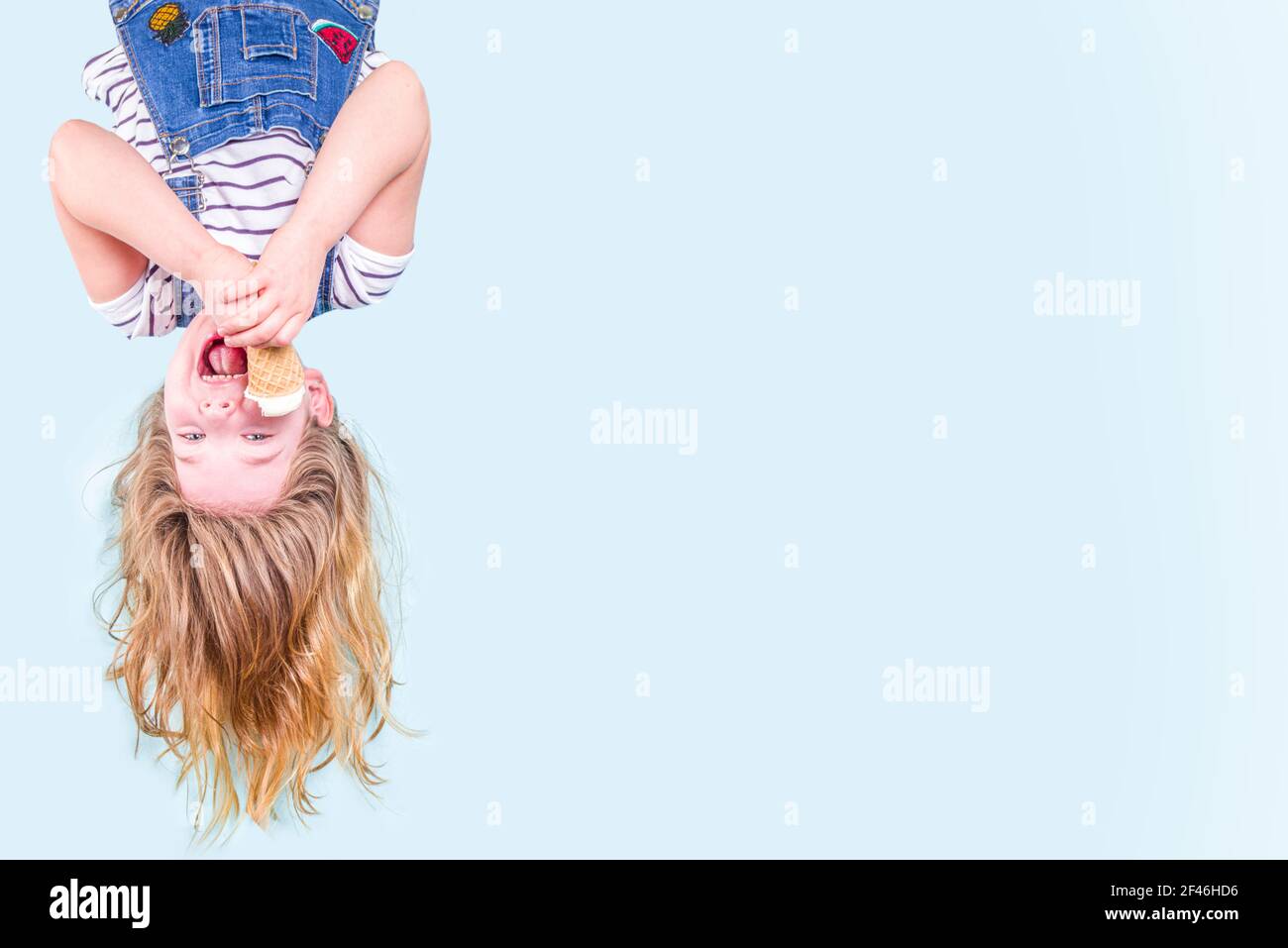 Cute fröhlich glücklich Kleinkind Kind Mädchen auf den Kopf mit flatternden Haaren, Essen Vanille Eis. Sommerurlaub Spaß Konzept auf blauem Hintergrund Kopie s Stockfoto