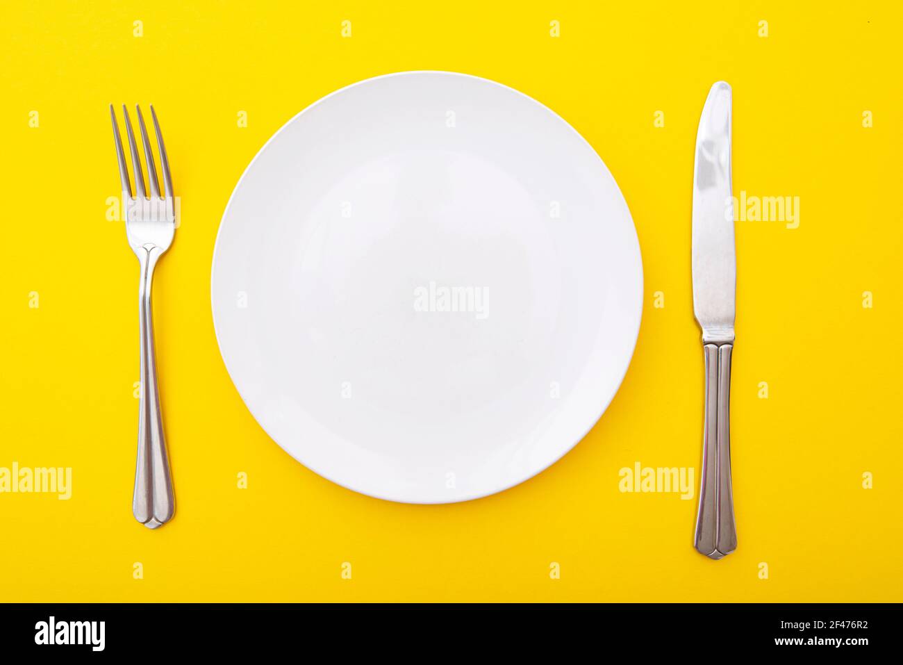 Weiße Keramikplatte mit Messer und Gabel auf gelber Oberfläche, Küchentisch, Layout, Draufsicht, Platz für Text Stockfoto