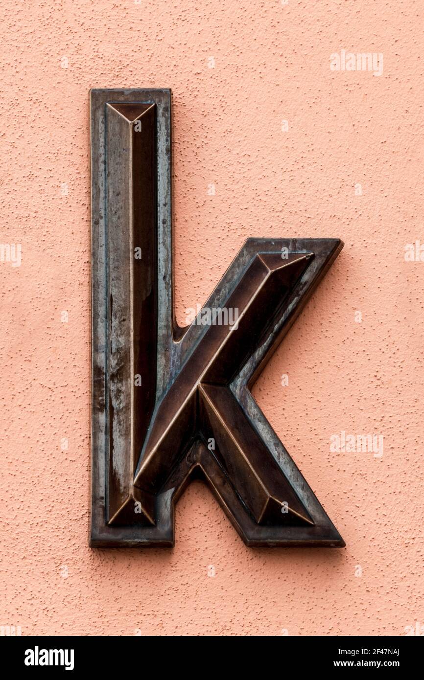 Dunkelbraun glasierte Buchstaben k auf einer leuchtend orangefarbenen Wand Stockfoto