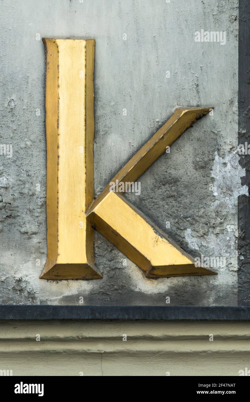 Historischer goldener Buchstabe K mit Serifen an einer grauen Wand Stockfoto