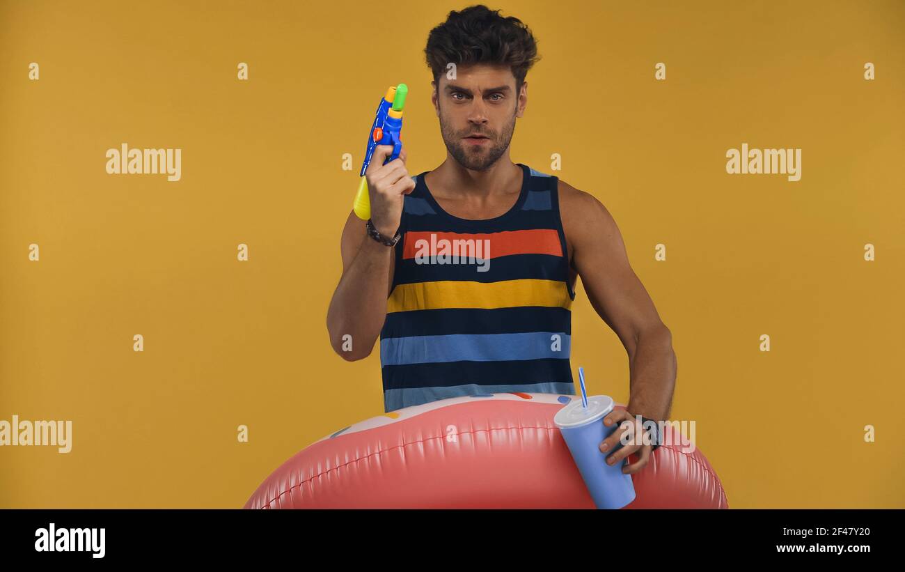 Mann im Schwimmring hält Pappbecher beim Spielen mit Wasserpistole auf gelb  isoliert Stockfotografie - Alamy