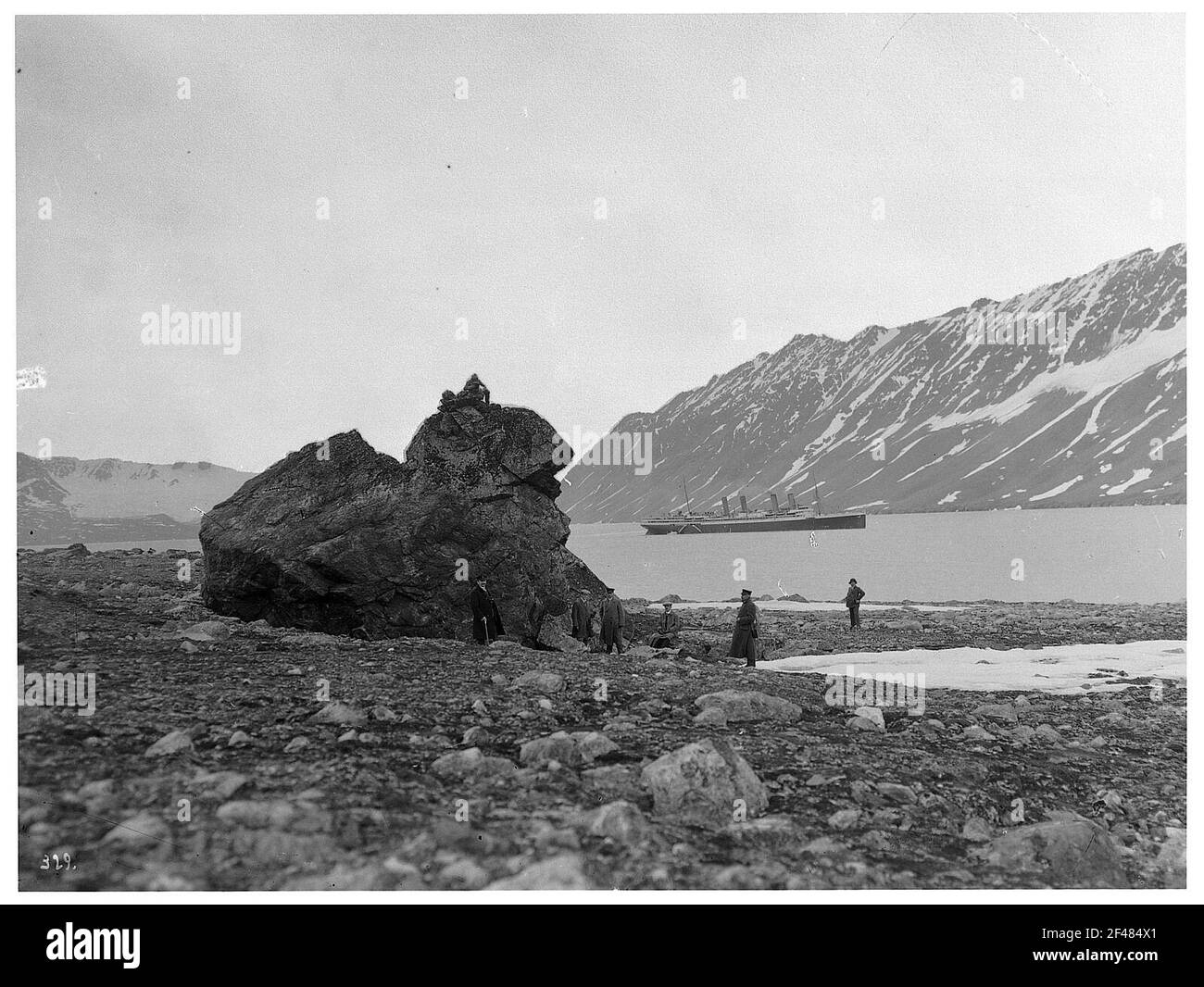 Spitzbergen, Norwegen. Crossbay. Touristen vor Felsformation am Steinufer der Kreutzbucht. Blick auf das gegenüberliegende Ufer mit dem Hochsee-Passagierdampfer 'Victoria Luise' auf Reede vor schneebedeckten Bergen Stockfoto