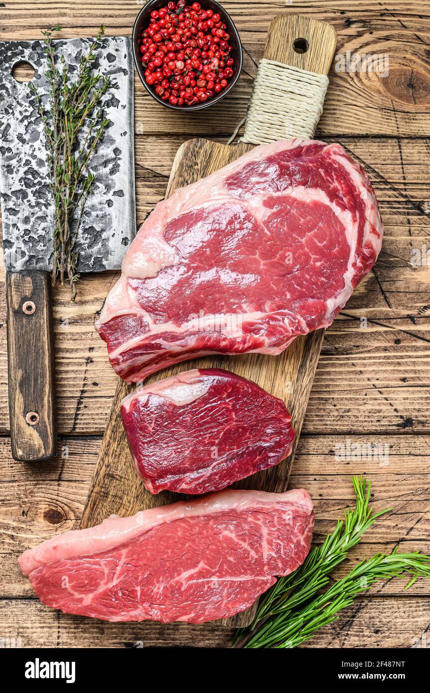 Frisch roh prime schwarz angus Rindfleisch Steaks Filet Mignon, Rib Eye oder Cowboy, Striploin. Holzhintergrund. Draufsicht Stockfoto