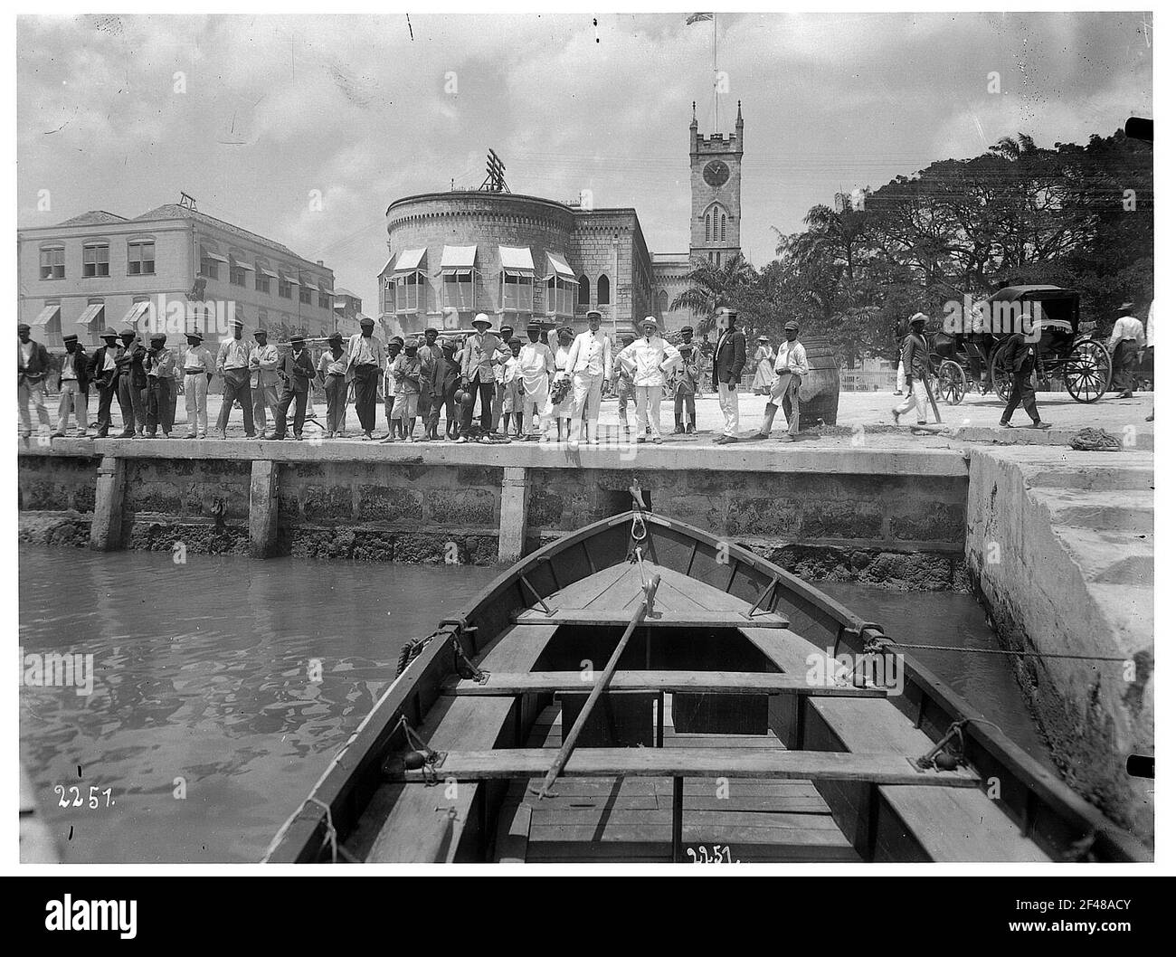 Barbados. Hafenszene mit Einheimischen und Touristen an der Kaimauer, im Hintergrund eine Kirche. Blick von einem Liegeplatz Ruderboot Stockfoto