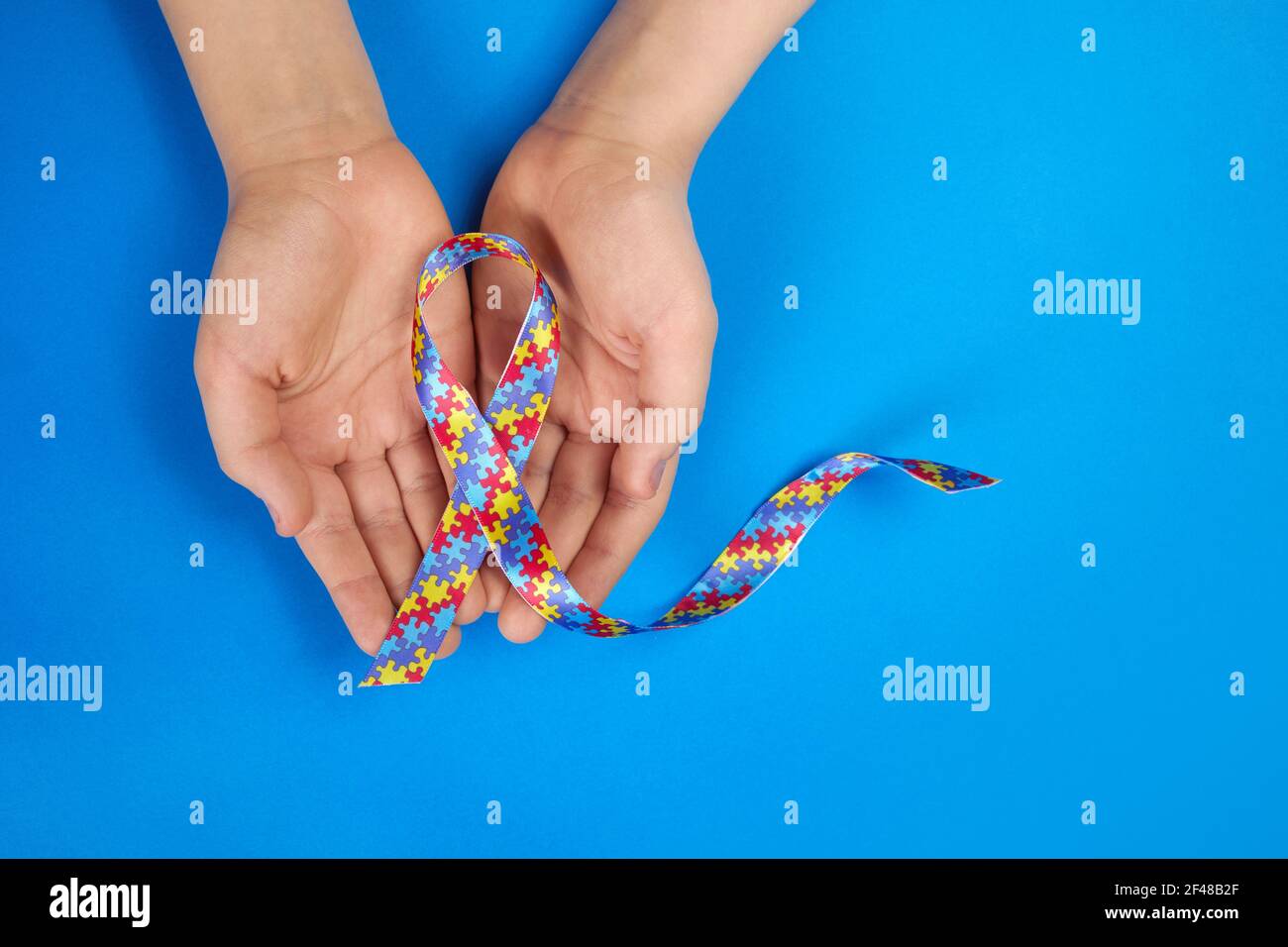 Welt Autismus Tag Bewusstsein. Autistische Jungen Hände halten Puzzle-Muster Band auf blauem Hintergrund Stockfoto