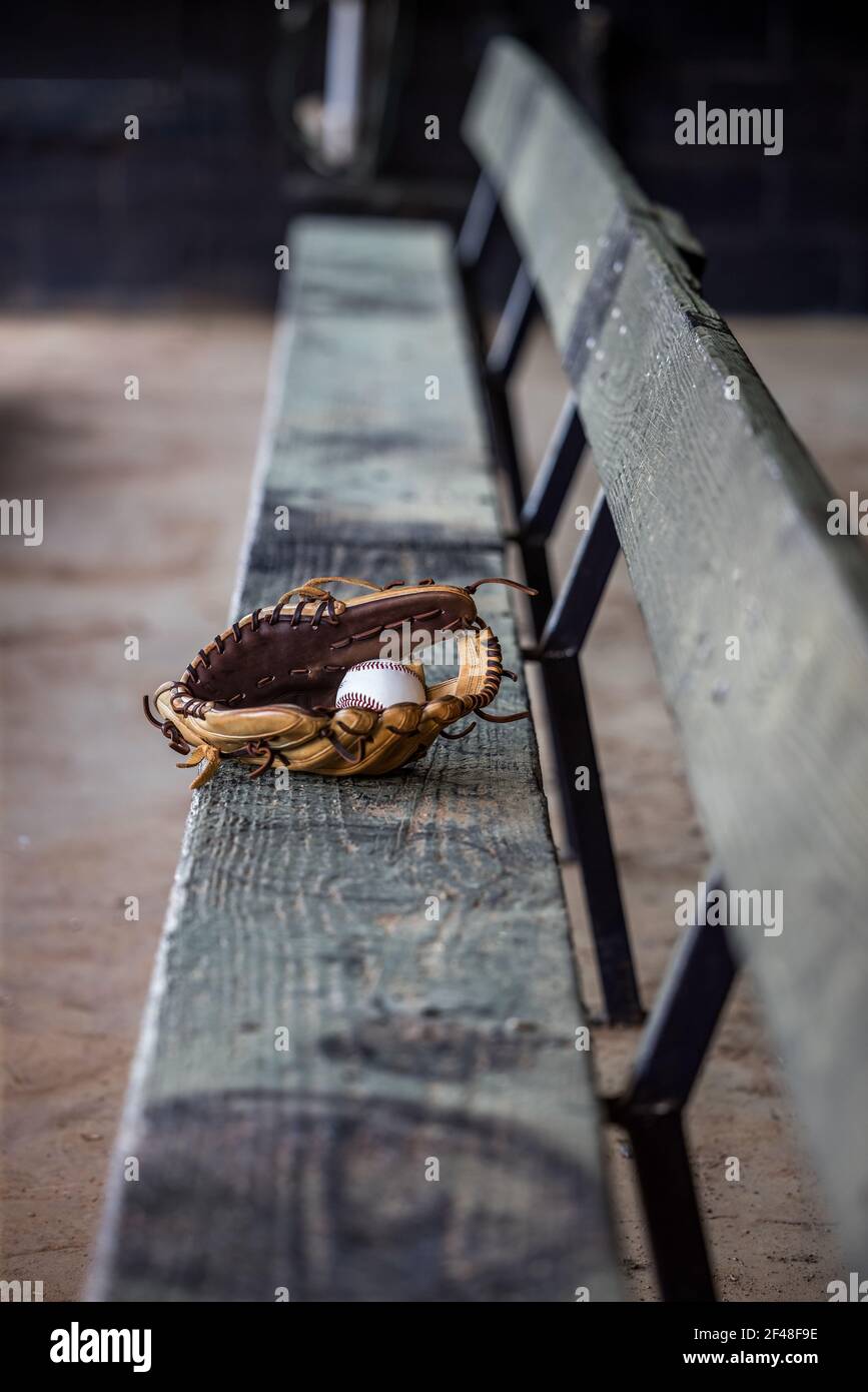 Leere ausgegrabene Bank an einem Baseballfeld mit einem einschläfenden Baseballhandschuh und Baseball in der Mitte sitzen. Stockfoto