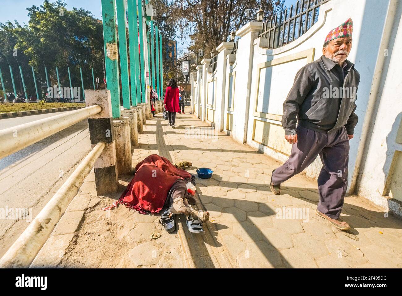 Nepalesischer Mann, der auf den Straßen von Kathmandu, Nepal, an einem an Lepra leidenden Bettler vorbeigeht Stockfoto