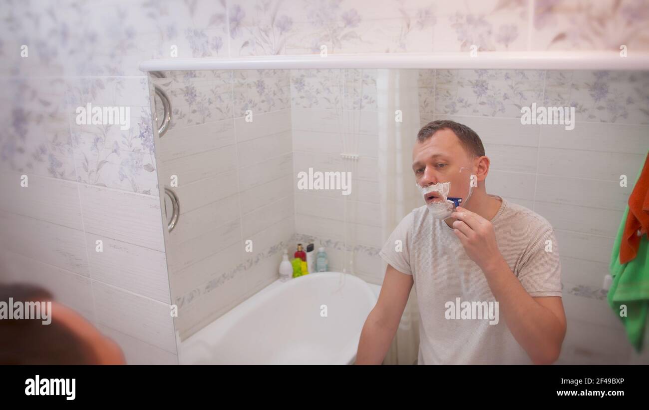 Junger Mann rasiert, während er im Badezimmer vor dem Spiegel steht, Rückansicht Stockfoto